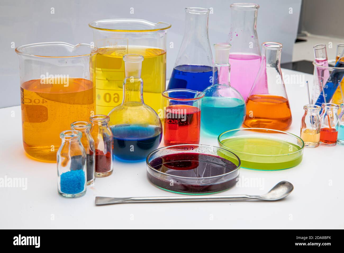 Verrerie de laboratoire avec des liquides de différentes couleurs sur table blanche. Verrerie de laboratoire volumétrique sur fond blanc. Banque D'Images