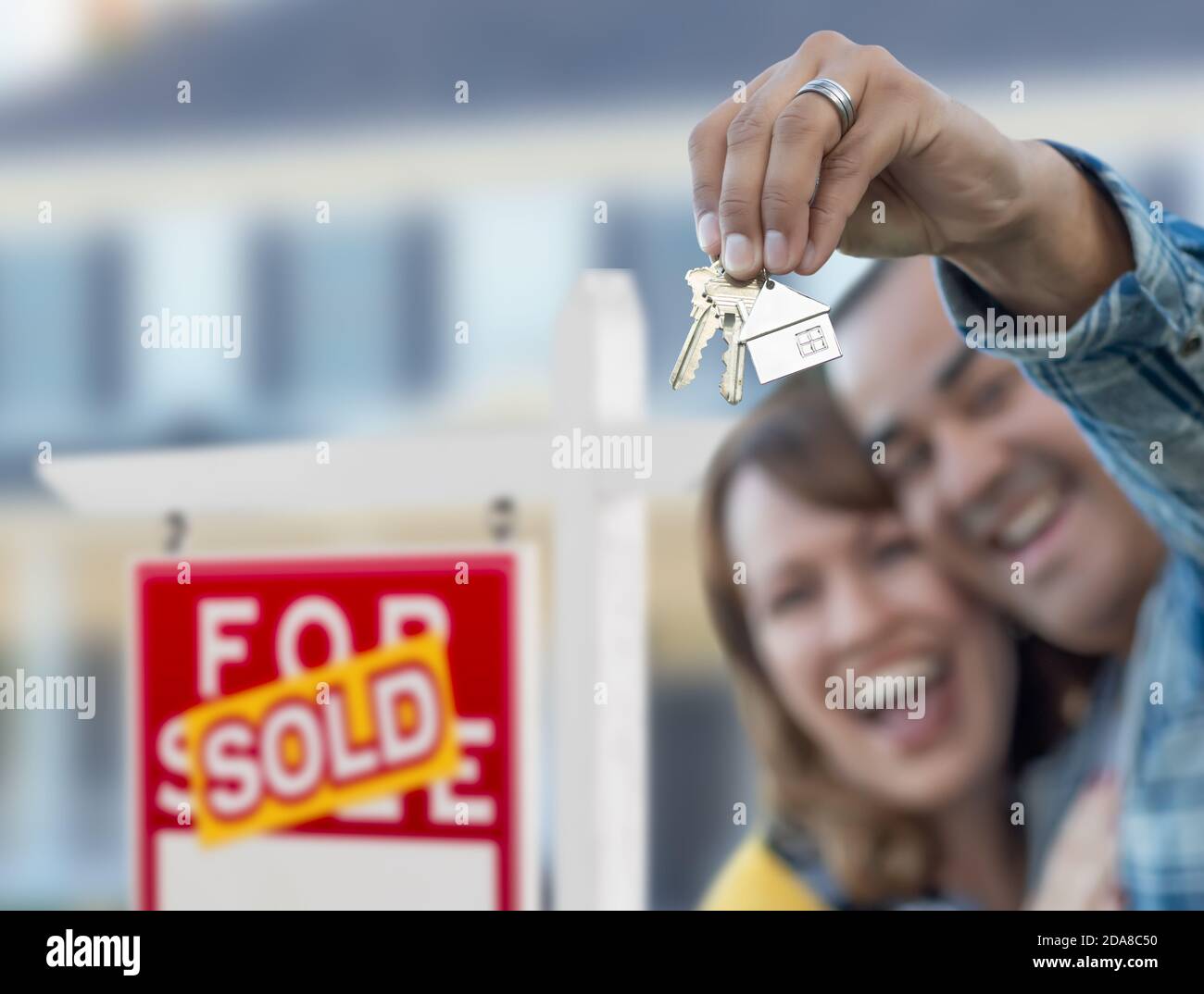 Couple de course mixte devant l'enseigne de l'immobilier vendu et la maison avec des clés. Banque D'Images