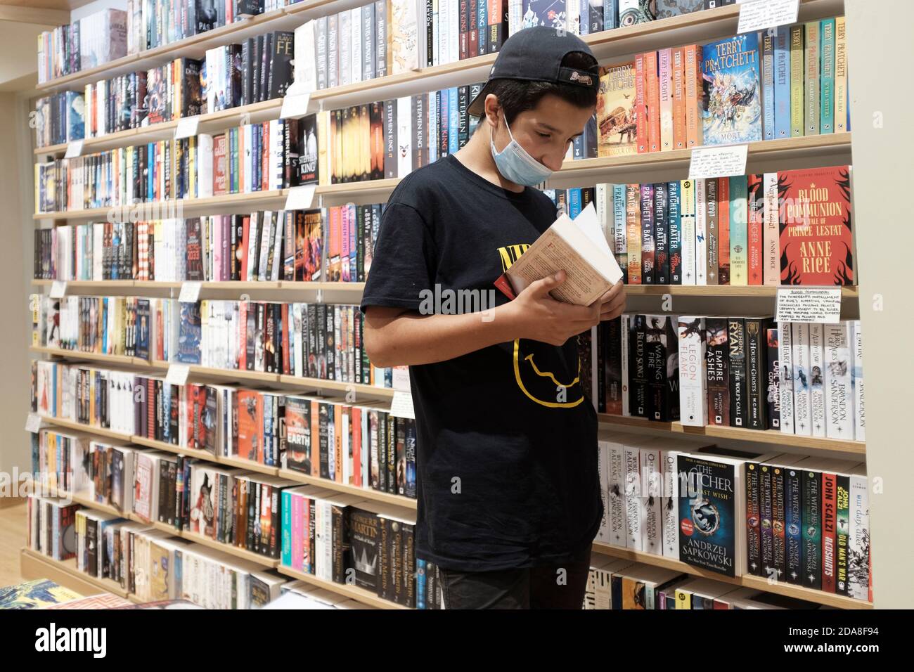 Teenage Boy, 13-14 ans, Wearing gace masque choisir des livres dans la librairie, Londres, Royaume-Uni Banque D'Images