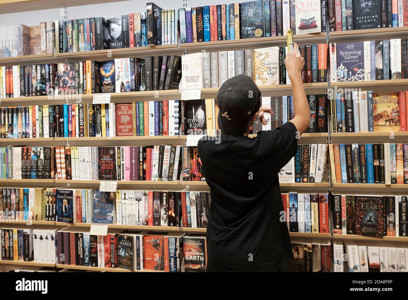 Teenage Boy, 13-14 ans, Wearing gace masque choisir des livres dans la librairie, Londres, Royaume-Uni Banque D'Images