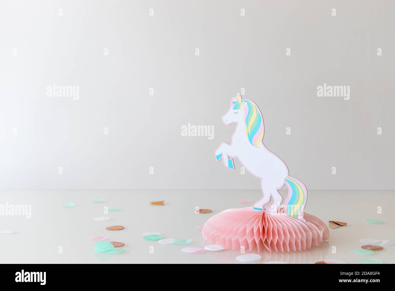 Décoration de fête des filles avec une licorne en papier et des points confetti sur une table en verre, fond blanc et uniforme Banque D'Images