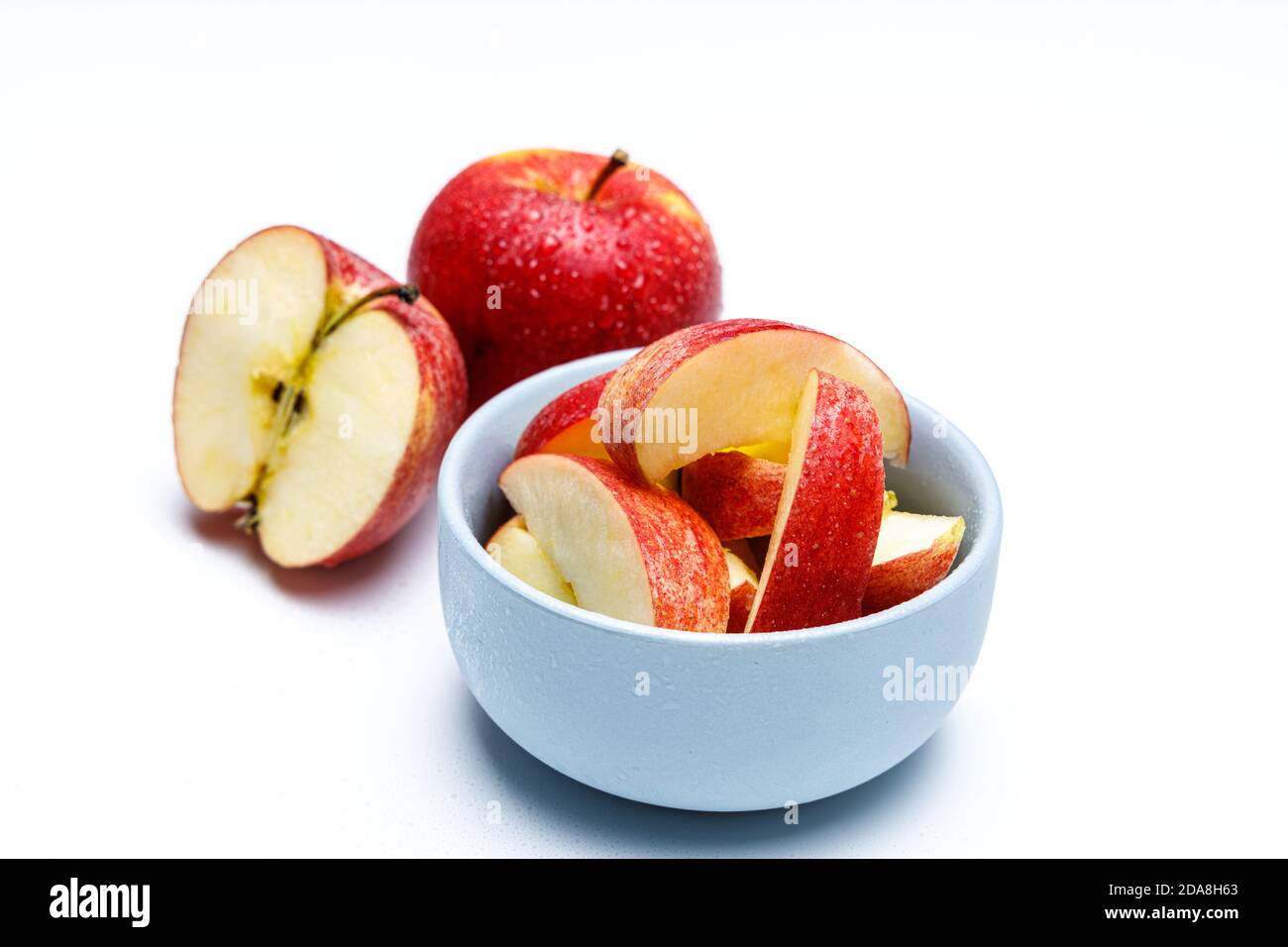 Vue de dessus des tranches de pomme dans un bol en céramique bleu clair avec deux pommes en arrière-plan, l'une est coupée en deux, des éclaboussures d'eau et des gouttes Banque D'Images