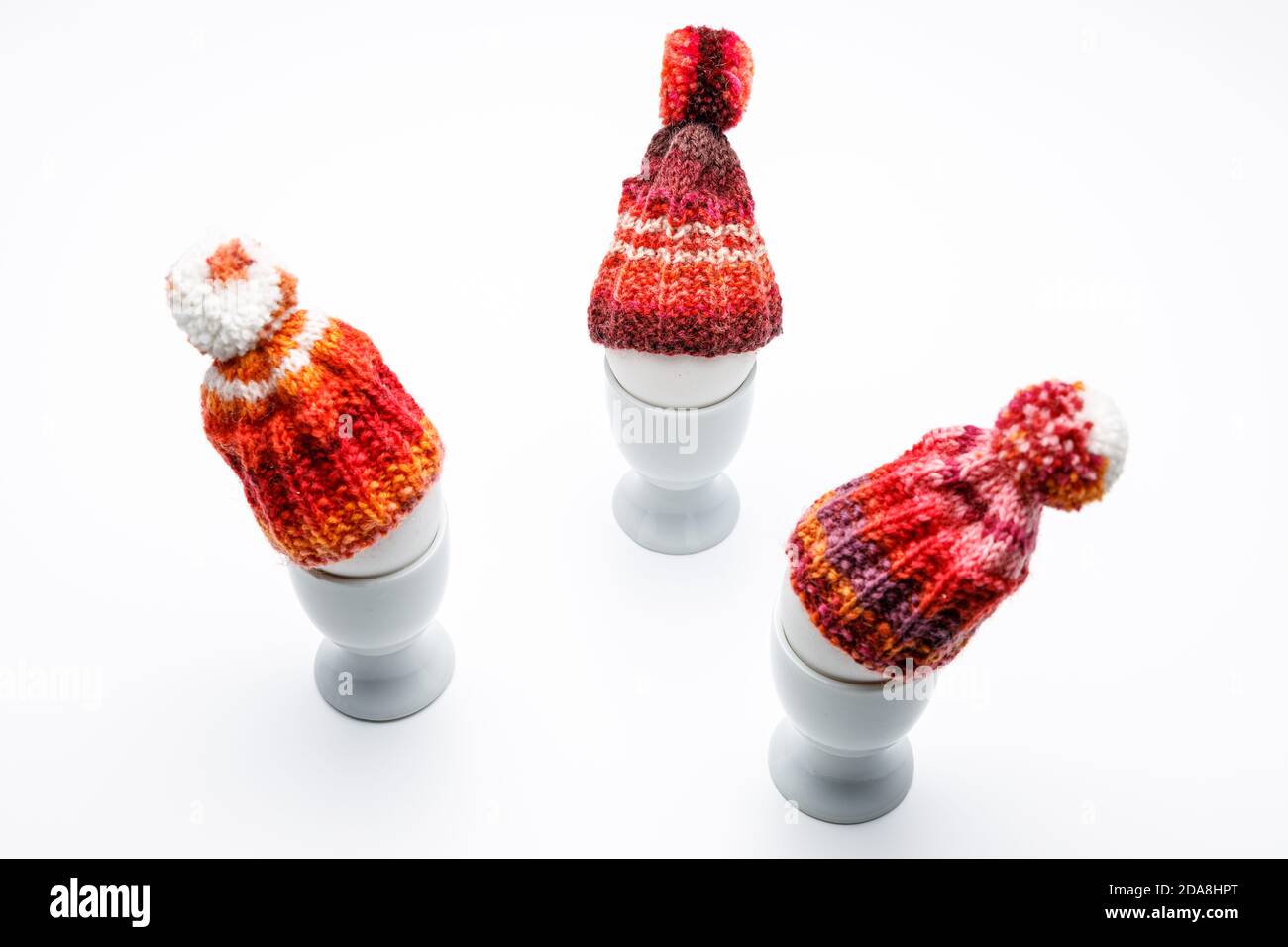 trois têtes d'œufs dans une coupe d'œuf dans une discussion, vêtues d'un bonnet en laine rouge orange sur un fond gris foncé et d'une table blanche, à utiliser pour le salut de pâques c Banque D'Images