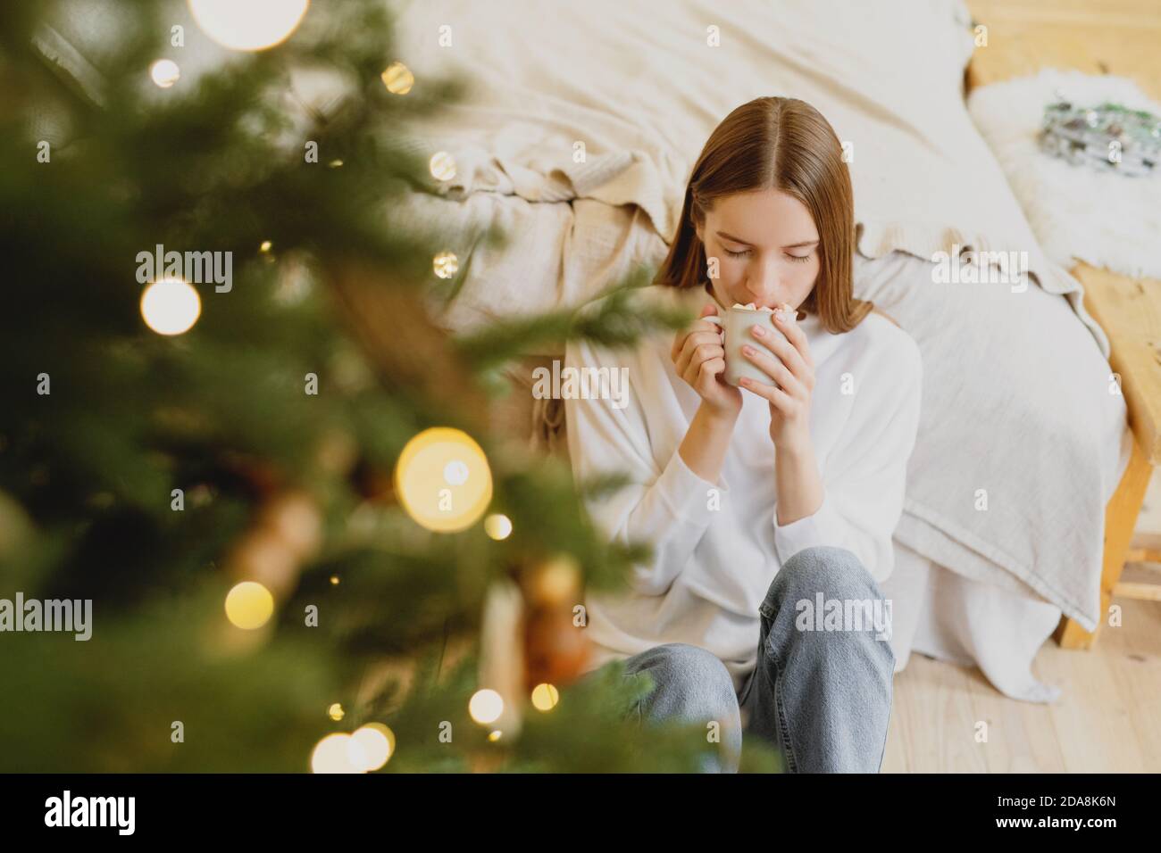 Jeune belle femme avec les yeux fermés boire du chocolat chaud avec guimauve dans la maison décorée de noël. Banque D'Images