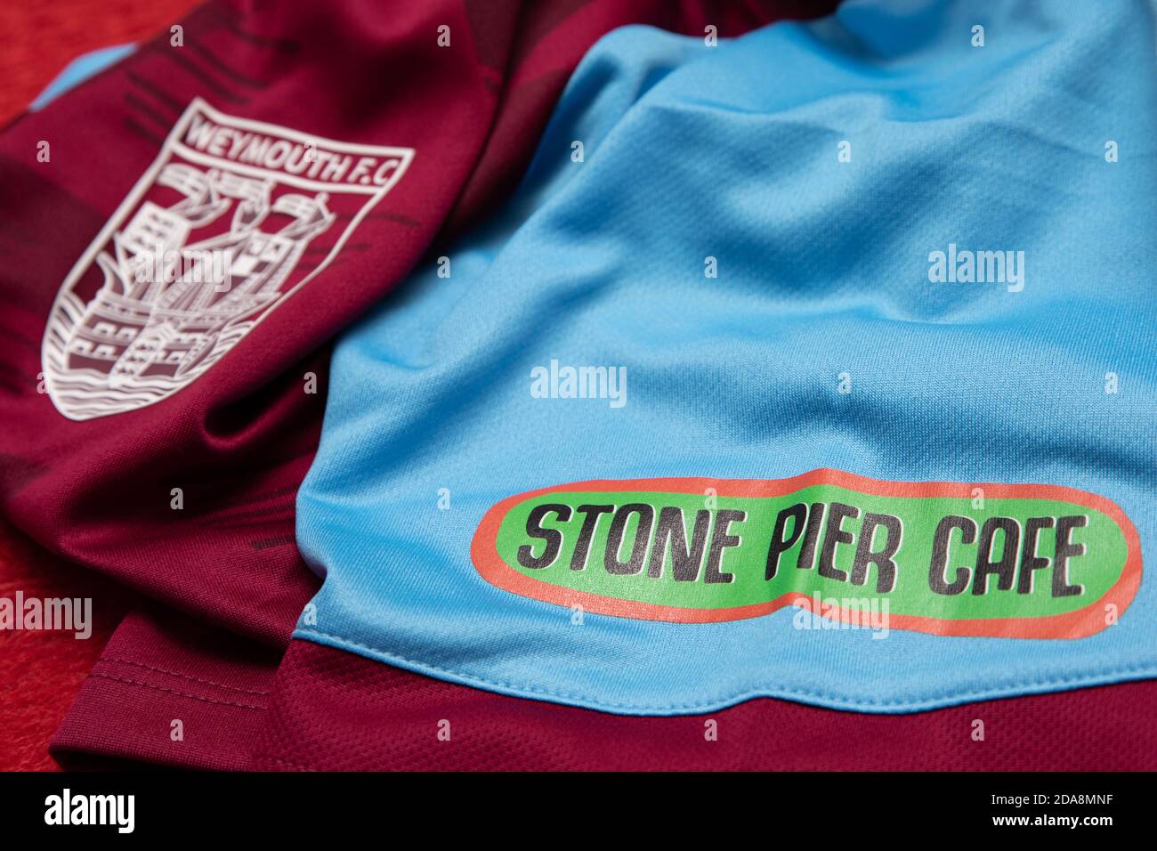 Logo de parrainage Stone Pier Cafe à côté de l'insigne du Weymouth football Club sur le maillot domicile pour Femme de Weymouth FC. Banque D'Images