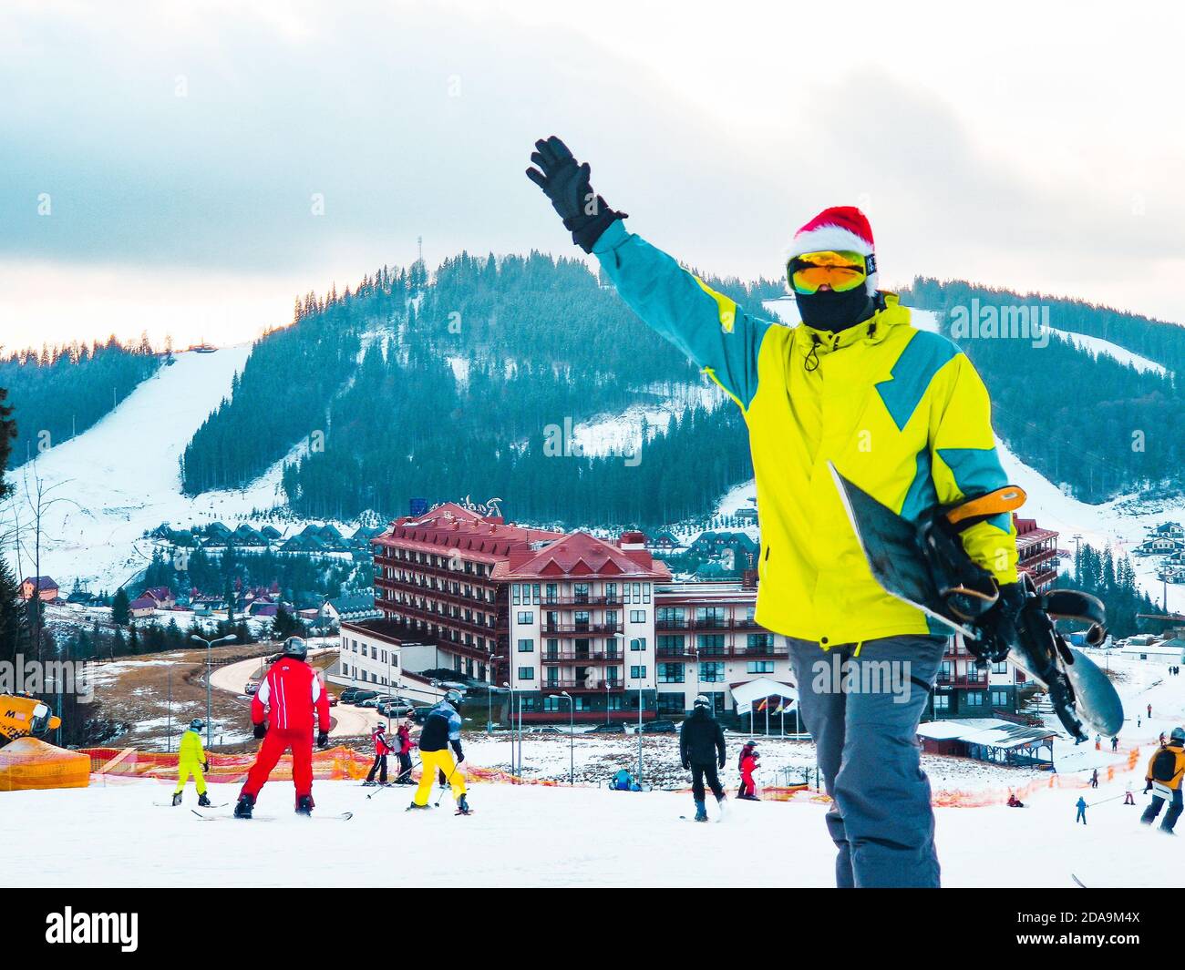 Homme avec snowboard à red christmas hat walking up par neigé hill Banque D'Images