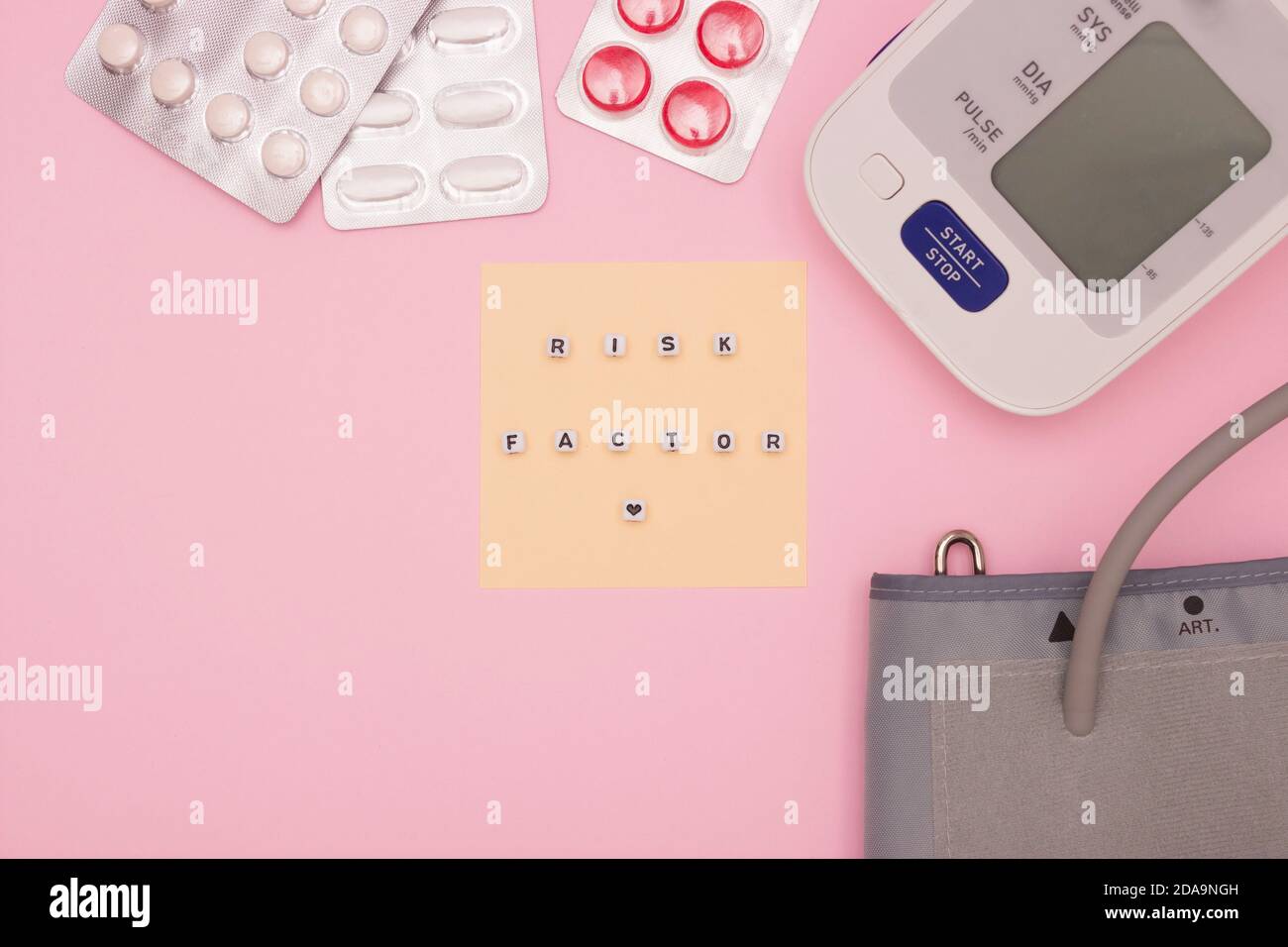 Concept de santé, cardiologie, maladie cardiaque. Les mots « FACTEUR DE RISQUE » sur les blocs. Moniteur de tension artérielle, comprimés sur fond rose. Vue de dessus, f Banque D'Images