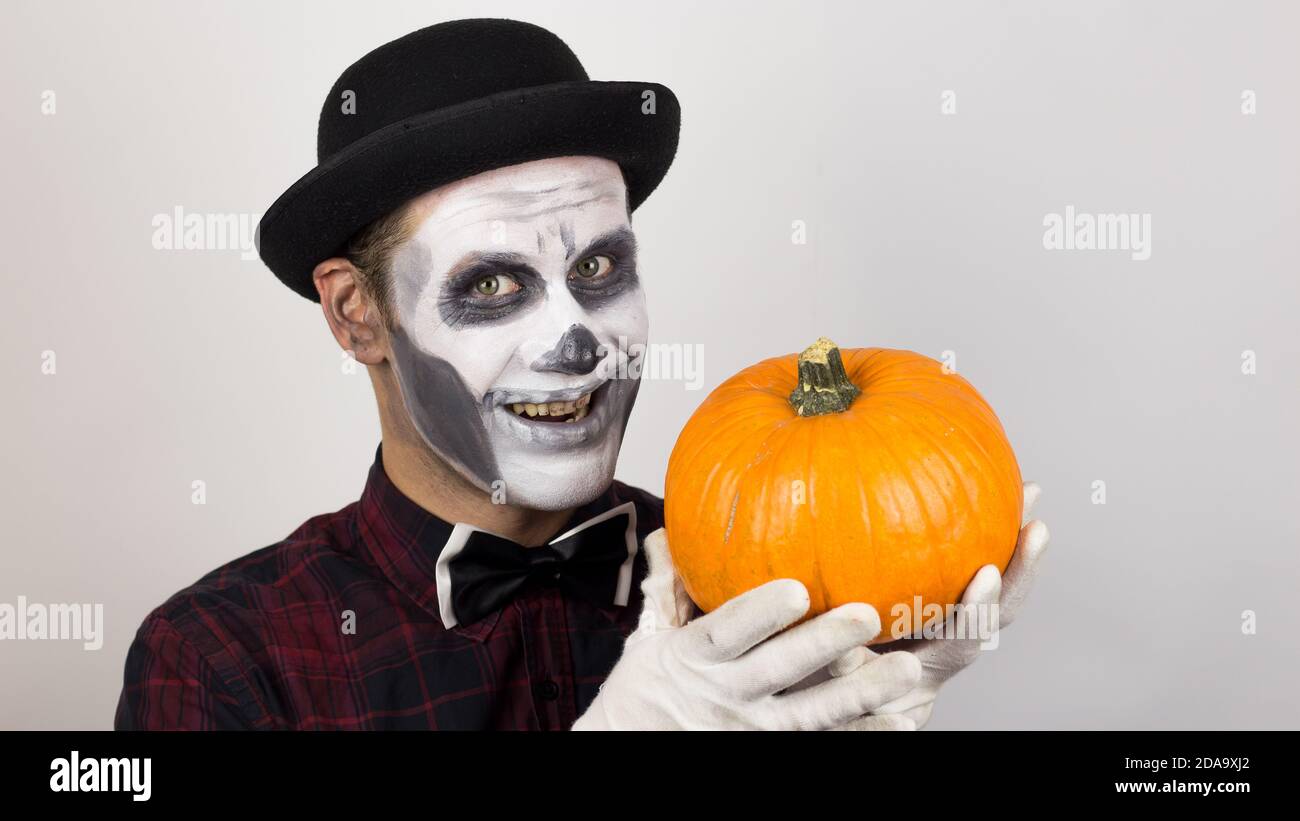 Un clown effrayant regarde la caméra, tient une citrouille dans ses mains et la menace avec un couteau. Costume d'Halloween. Banque D'Images