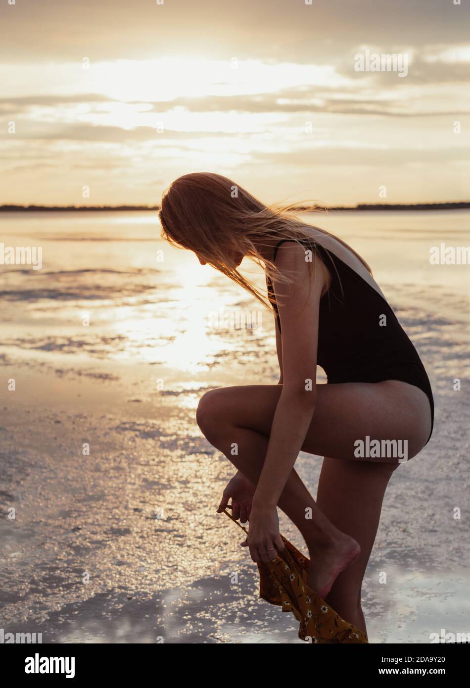 Belle jeune blonde avec des robes longues cheveux sur le bord du lac. Marchez pendant le coucher du soleil. Banque D'Images