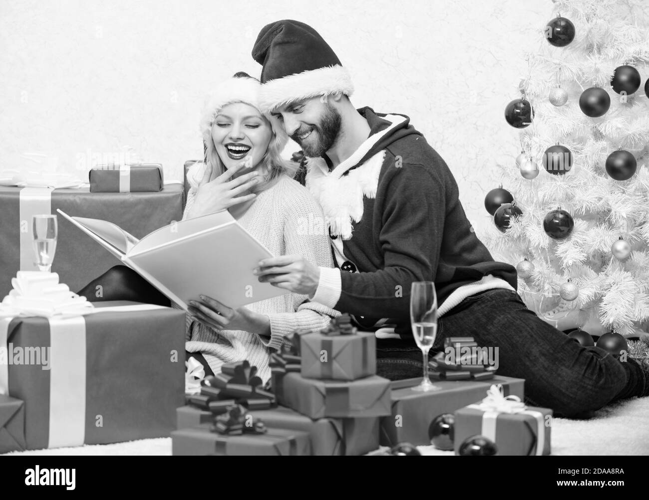 Un câlin familial boit du champagne près de l'arbre de noël tout en regardant un album photo de famille. Souvenez-vous des moments forts de l'année. Fêtez la nouvelle année ensemble. Tradition familiale. Couple amoureux aiment noël. Banque D'Images