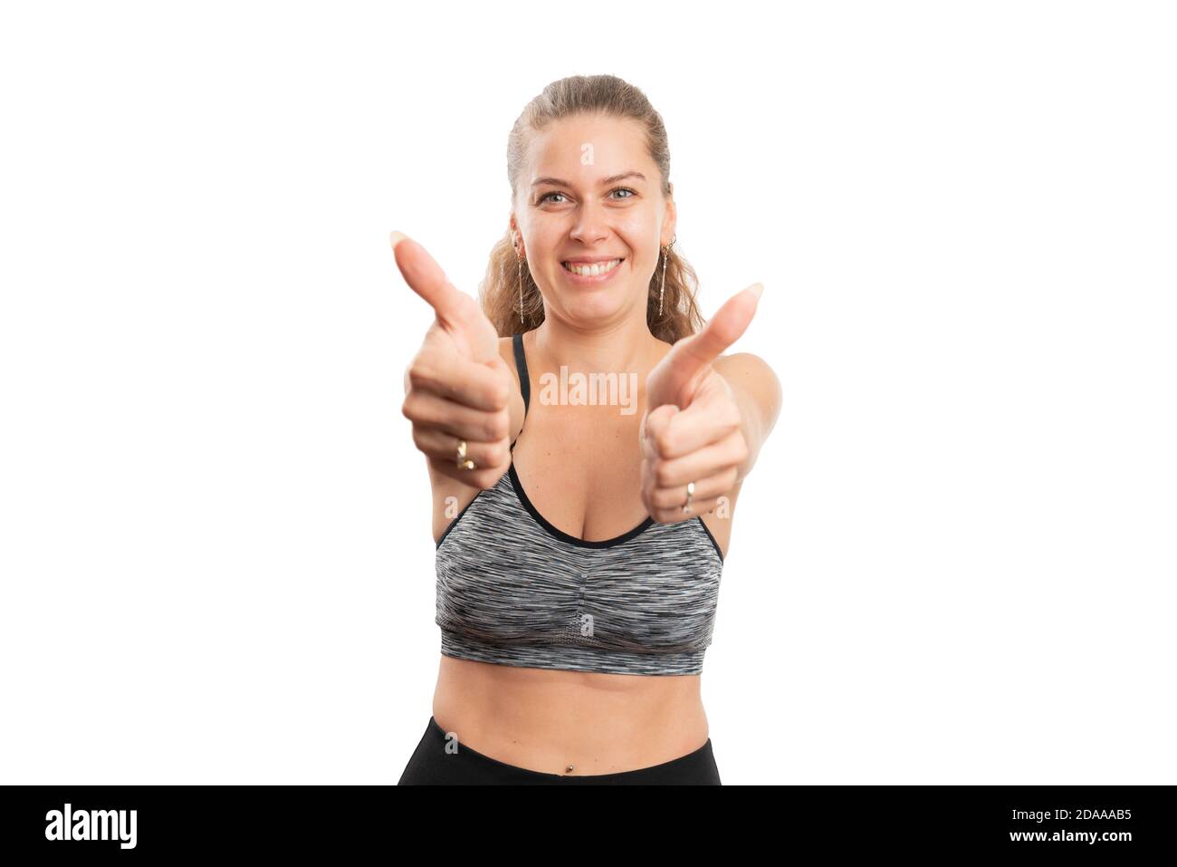 Femme adulte souriant faisant le double pouce-up comme un geste dans la salle de gym entraînement sportswear comme d'accord avec le concept sportif sain de style de vie isolé sur blanc Banque D'Images