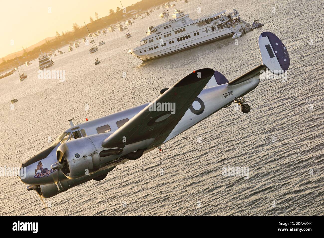 Un air à l'air d'un double moteur RAAF restauré, Beech 18 Expeditor avion volant bas au-dessus de la mer près d'un navire de voyage. Banque D'Images
