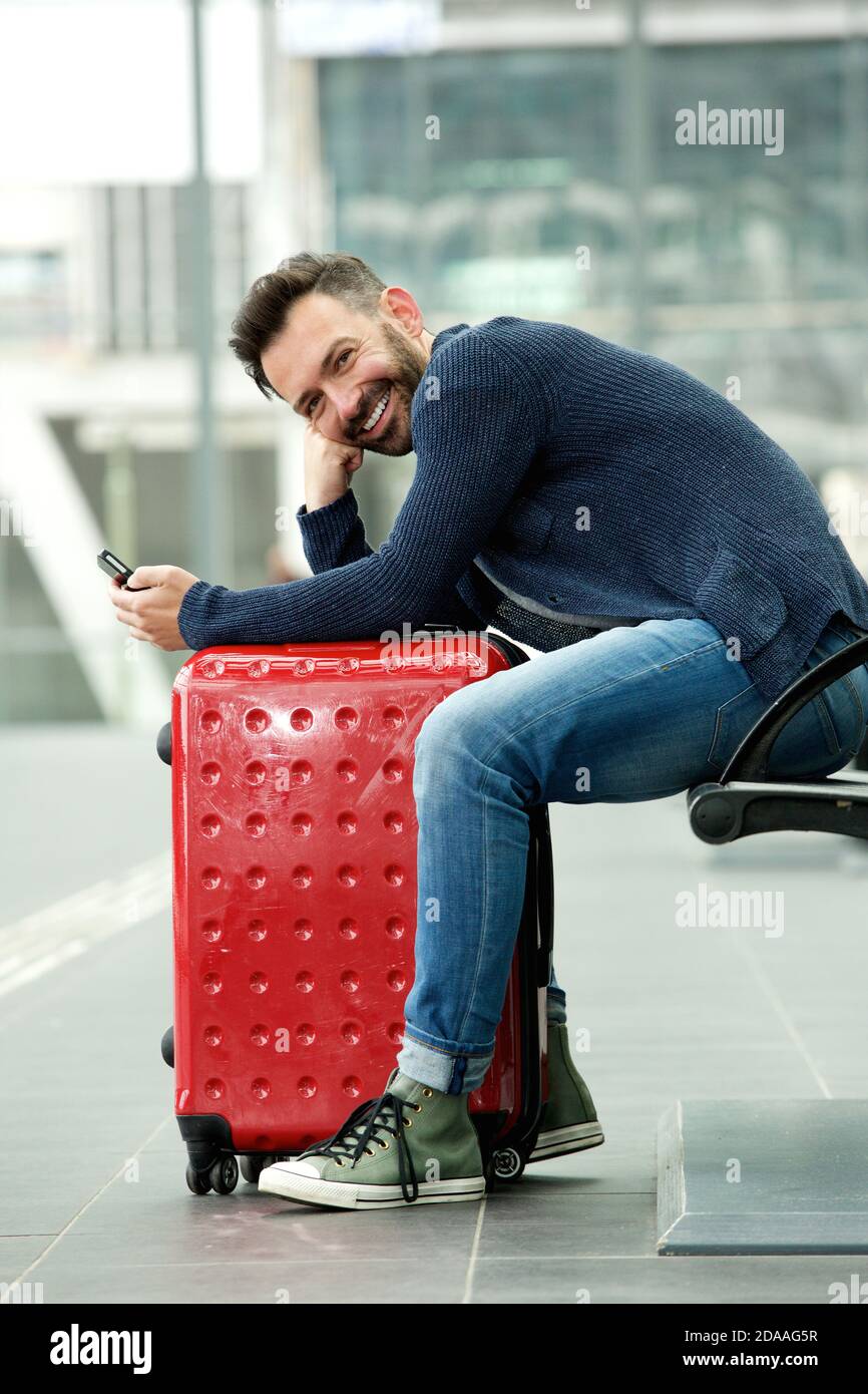 Portrait d'un beau homme d'âge moyen assis à la gare avec sac et téléphone portable Banque D'Images