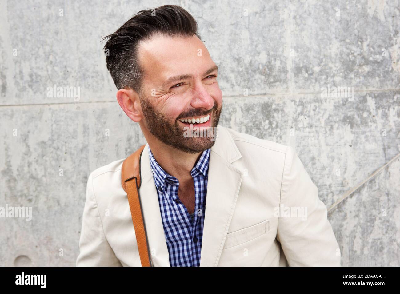 Portrait en gros plan d'un homme joyeux d'âge moyen avec barbe debout contre le mur et souriant Banque D'Images