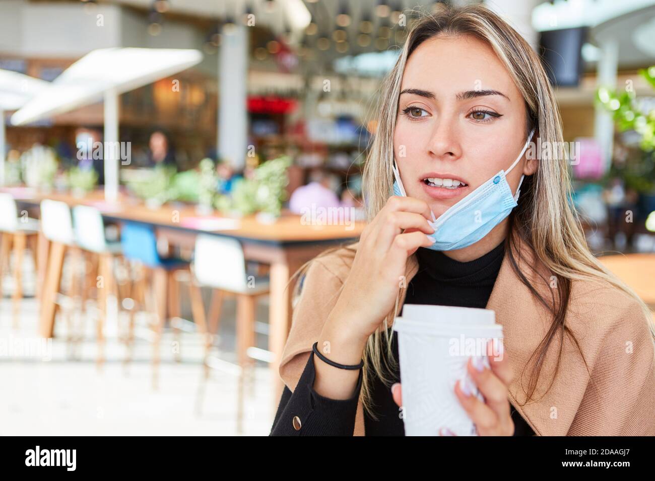 Une jeune femme en tant qu'invité dans le centre commercial avec une tasse à café et un masque pour le visage son menton Banque D'Images