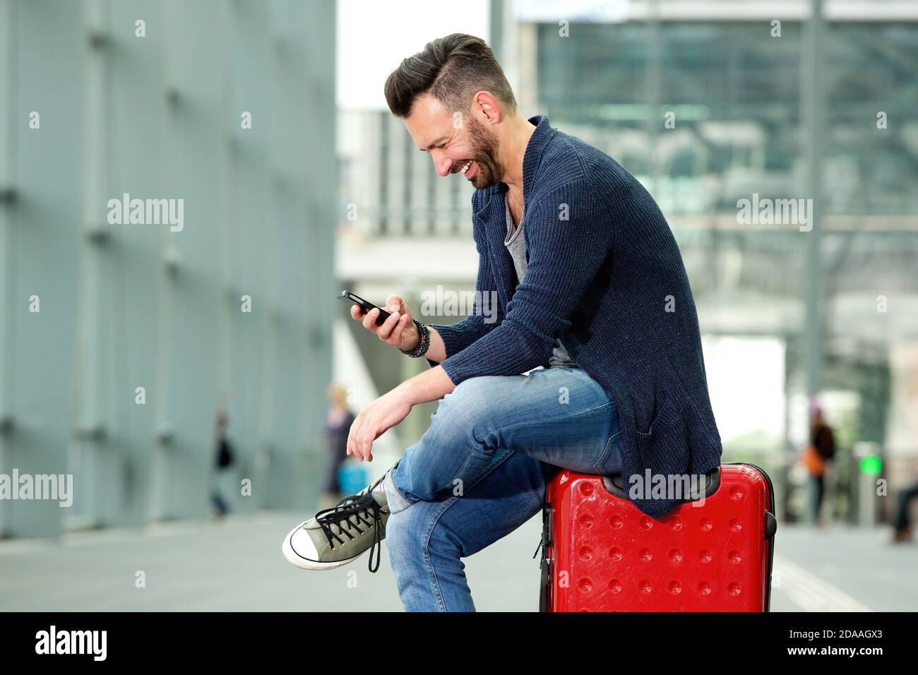 Portrait latéral d'un homme mûr heureux assis dans un sac de voyage et regarder le téléphone portable Banque D'Images