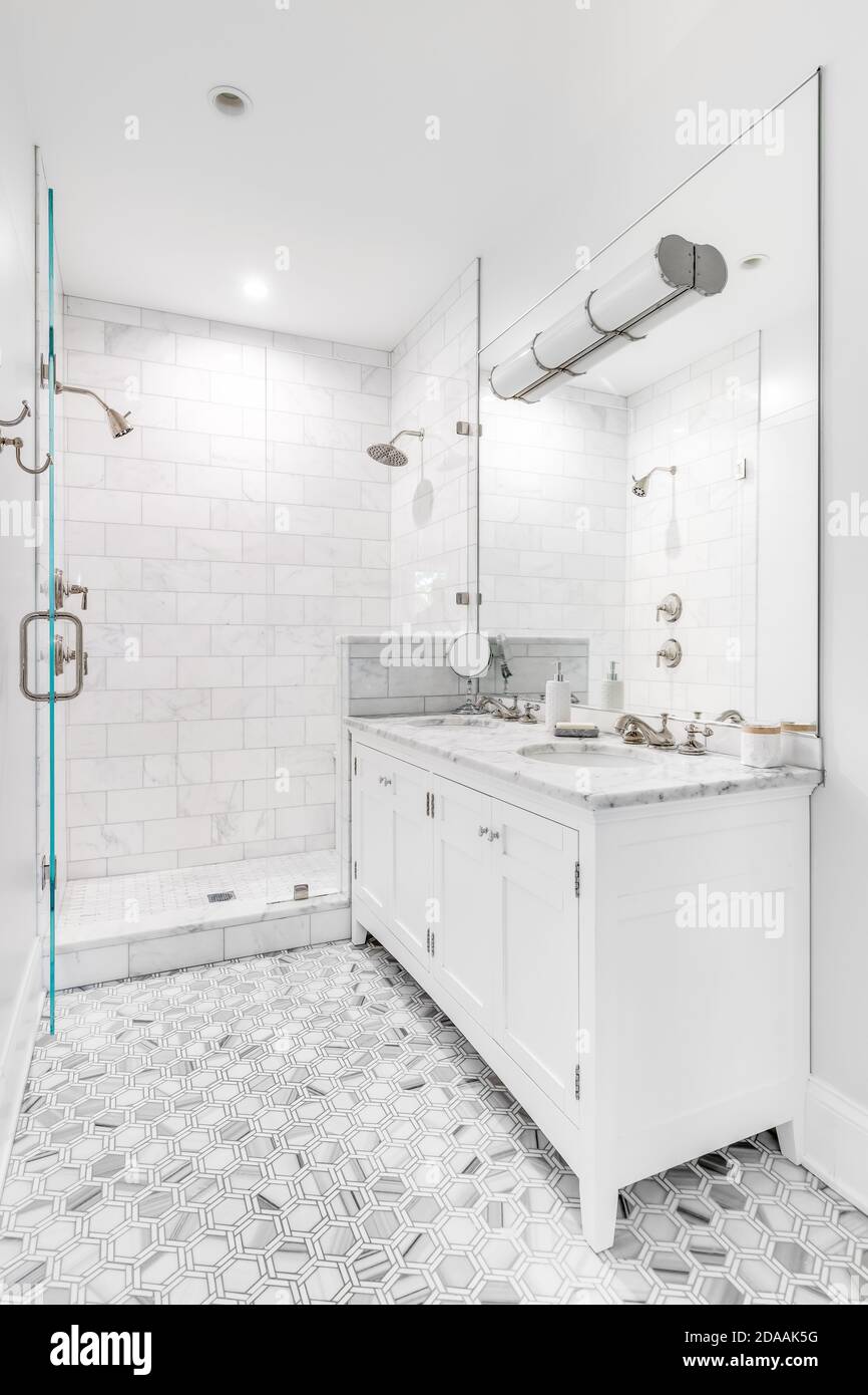 Une belle salle de bains blanche rénovée avec carrelage en marbre polygone gris au sol, douche en verre avec carrelage en métro et accessoires/quincaillerie chromés. Banque D'Images