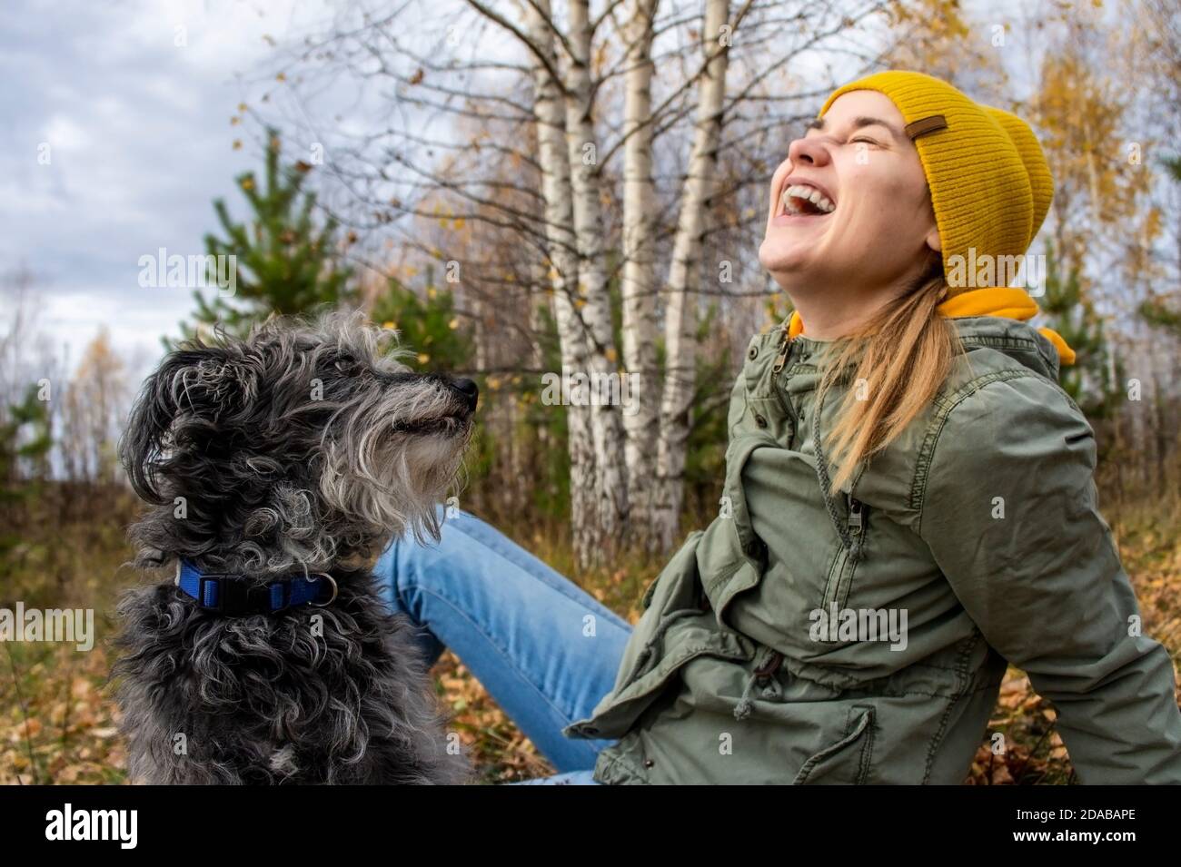 Jeune femme riant jouant avec son chien bien-aimé moelleux dans la forêt d'automne. Marcher avec les animaux de compagnie, les soins et l'amitié, les émotions positives. Saison d'automne Banque D'Images