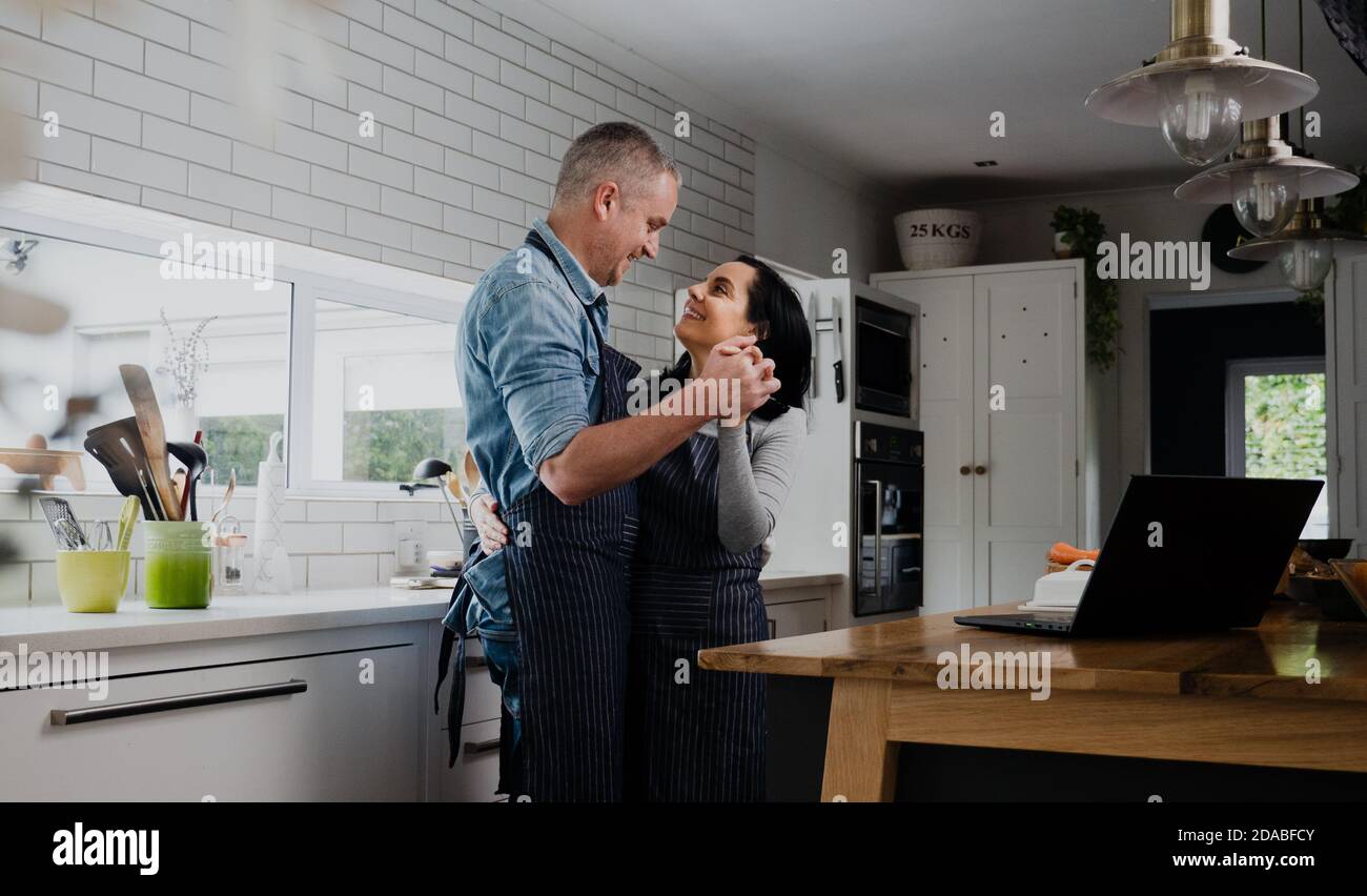 Couple heureux souriant tout en dansant lentement dans la cuisine préparant le dîner pour les enfants. Banque D'Images