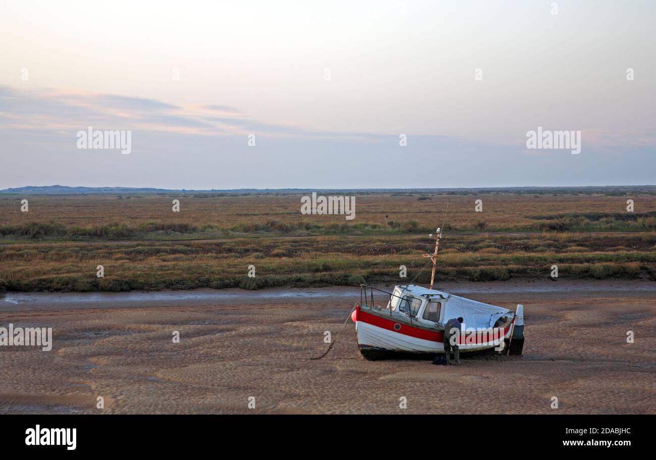 Un homme travaillant sur un bateau de pêche à basse eau dans le ruisseau Overy, sur la côte nord du Norfolk, à Burnham Overy Staitha, Norfolk, Angleterre, Royaume-Uni. Banque D'Images