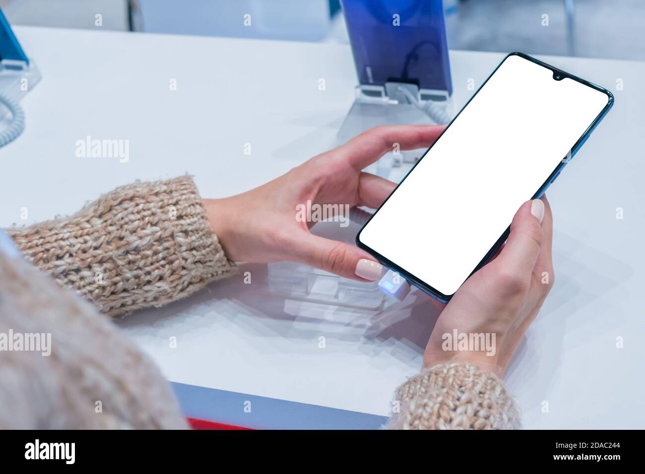 Image maquette: Femme client testant un nouveau modèle de smartphone avec un écran blanc vierge dans un magasin électronique, un salon de vente, une exposition. Maquette Banque D'Images