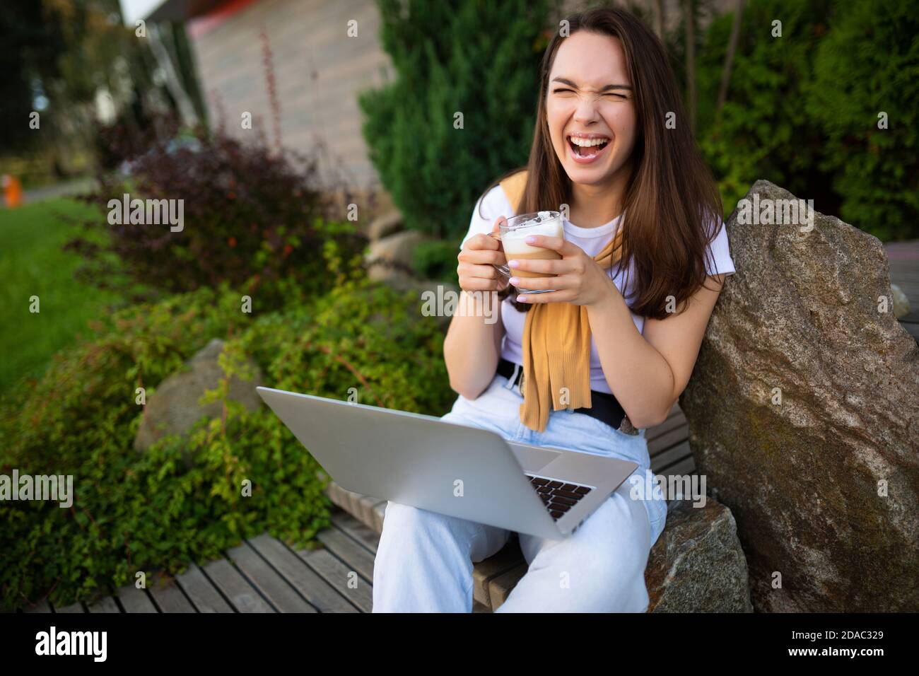 jolie jeune étudiante assise avec un ordinateur portable pendant la pause déjeuner assis à l'extérieur Banque D'Images