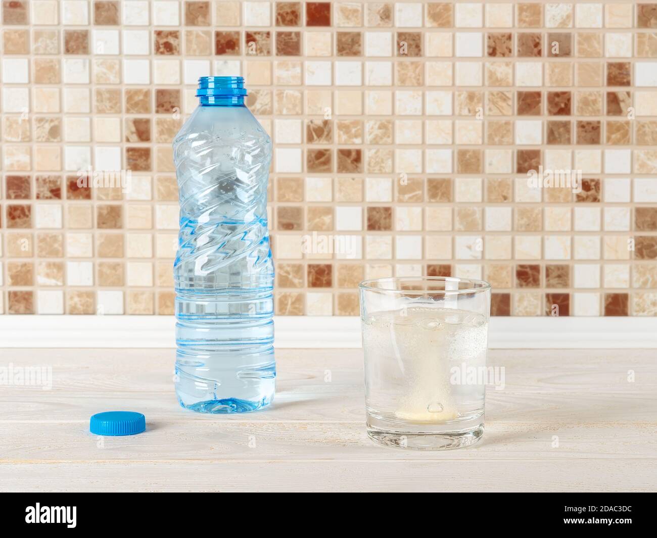 La vitamine effervescente commence à se dissoudre dans un verre d'eau potable pure sur une table en bois blanc. Vitamines et suppléments nutritionnels. Soif désaltérante. Banque D'Images