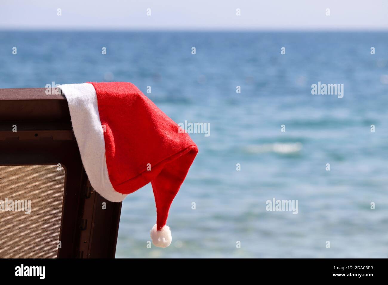 Noël sur une plage, fête du nouvel an sur une côte de mer. Chapeau de père Noël sur une chaise longue contre l'eau bleue Banque D'Images