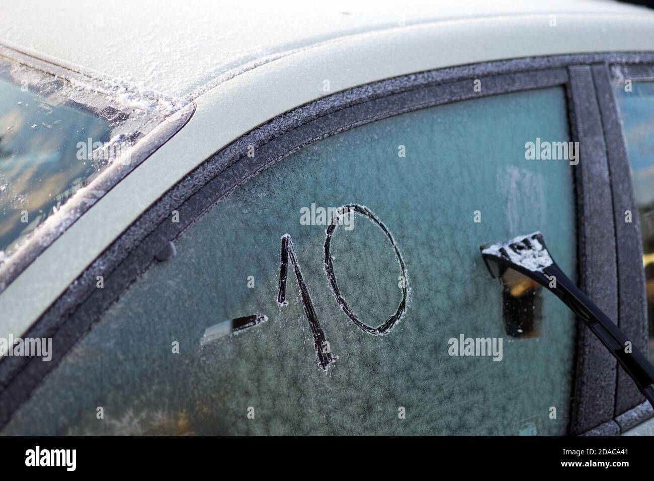 Vitre de voiture gelée avec texte rayé sur la glace : '-10' (moins dix) et outil de nettoyage Banque D'Images