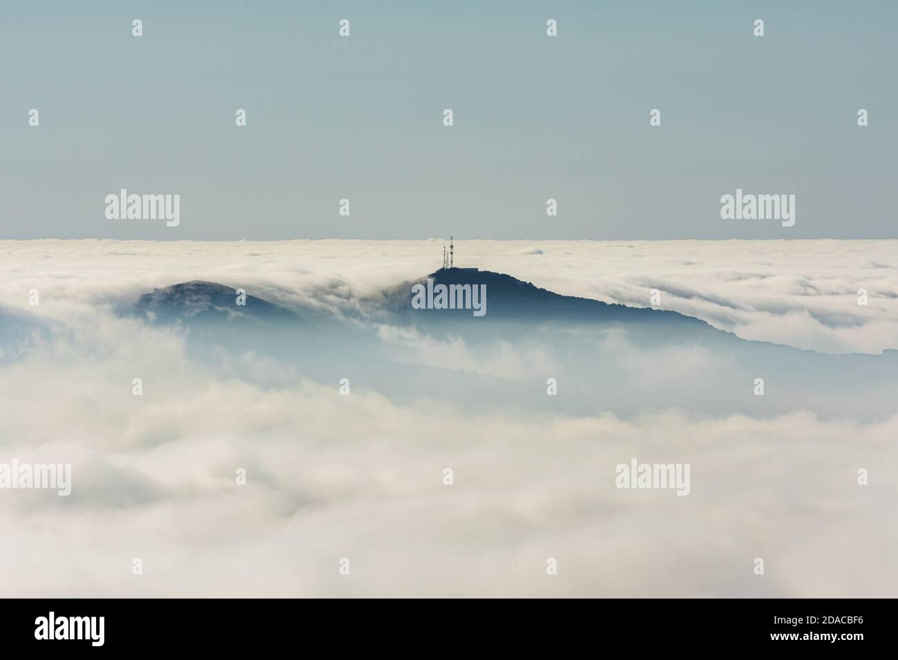 Montagne avec des antennes sur son sommet qui dépasse à travers les nuages, créant une île dans une mer de nuages. Banque D'Images