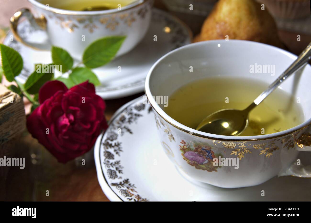 Gros plan de deux tasses à infusion avec décorations vintage à côté d'une rose, quelques muffins et quelques livres anciens Banque D'Images