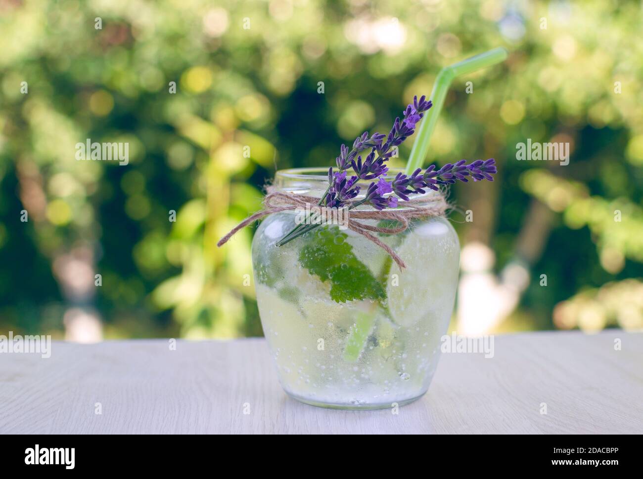 Pot en verre avec une limonade maison fraîche faite de menthe, de baume de citron, de citron, de lime, décorée de fleurs de lavande sur une table en bois dans le jardin Banque D'Images