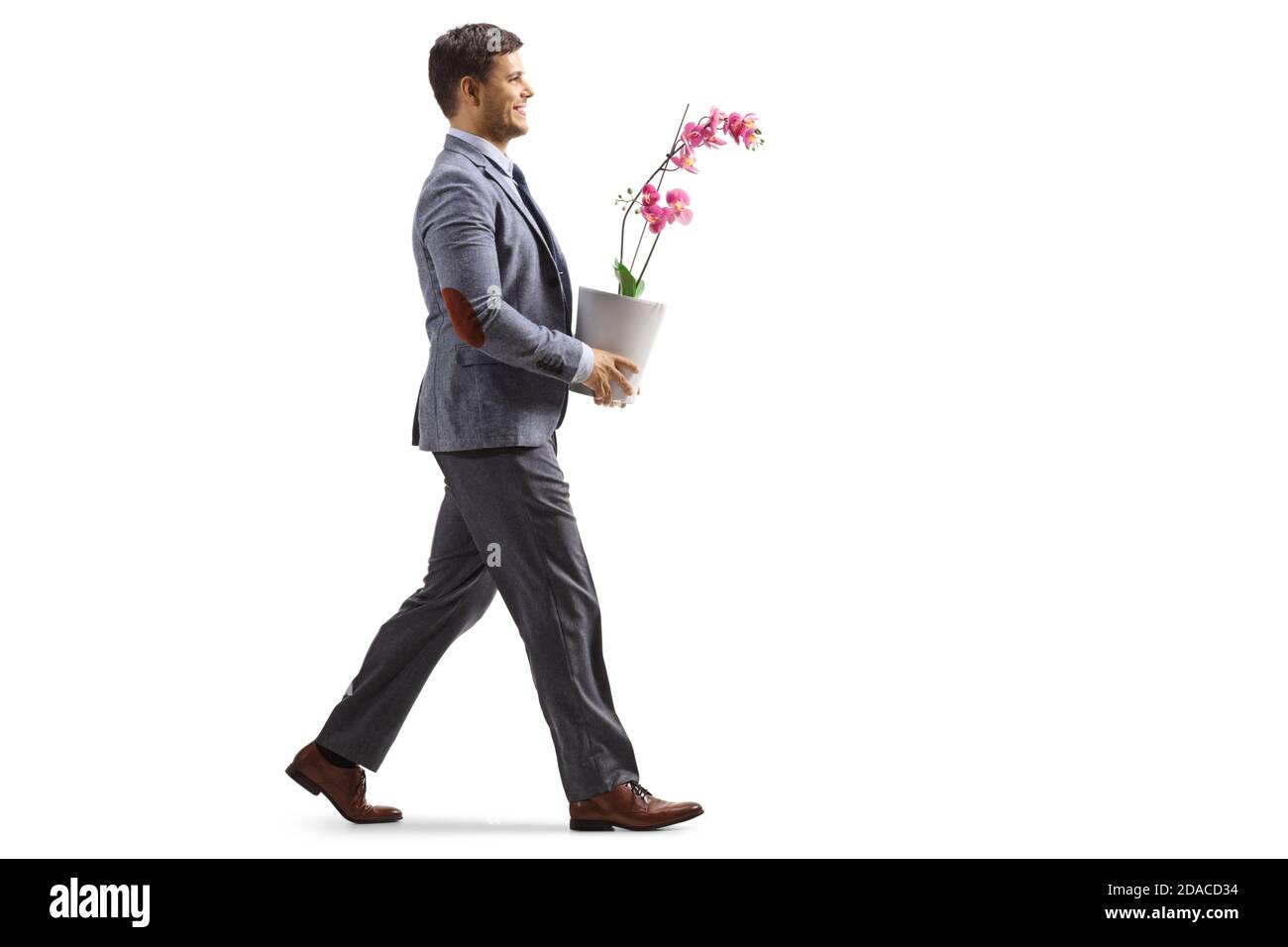 Prise de vue en coupe d'un jeune homme souriant un costume marchant un portant un pot de fleur d'orchidée isolé sur fond blanc Banque D'Images
