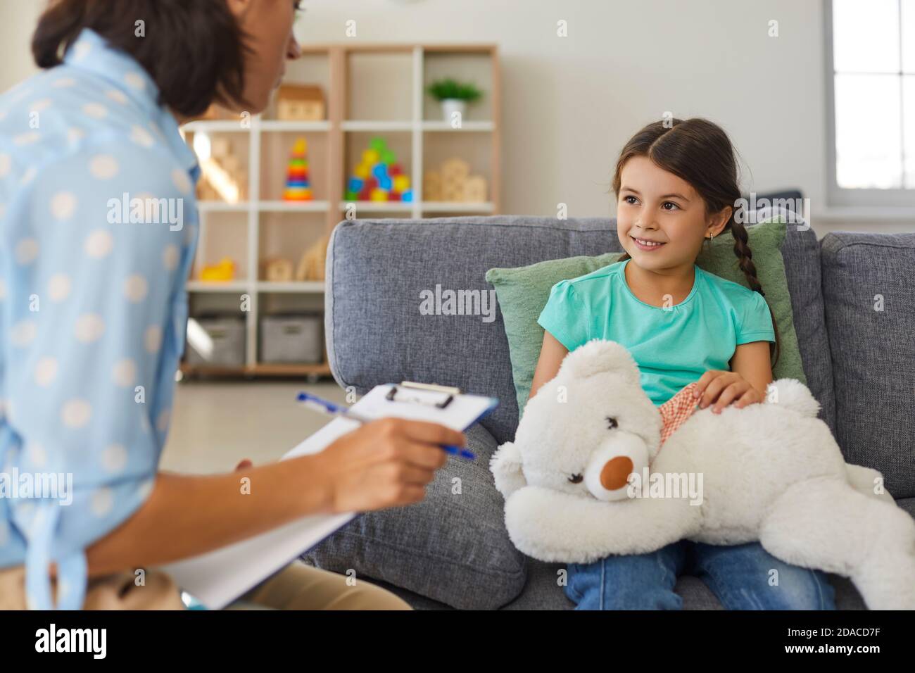 Petite fille mignonne parlant à l'enfant psychologue pendant la séance de thérapie dans un bureau moderne et confortable Banque D'Images