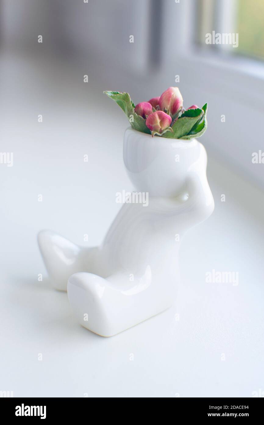 Figurine en céramique blanche de l'homme avec boutons de fleur de pomme sa tête est assise sur un rebord de fenêtre Banque D'Images