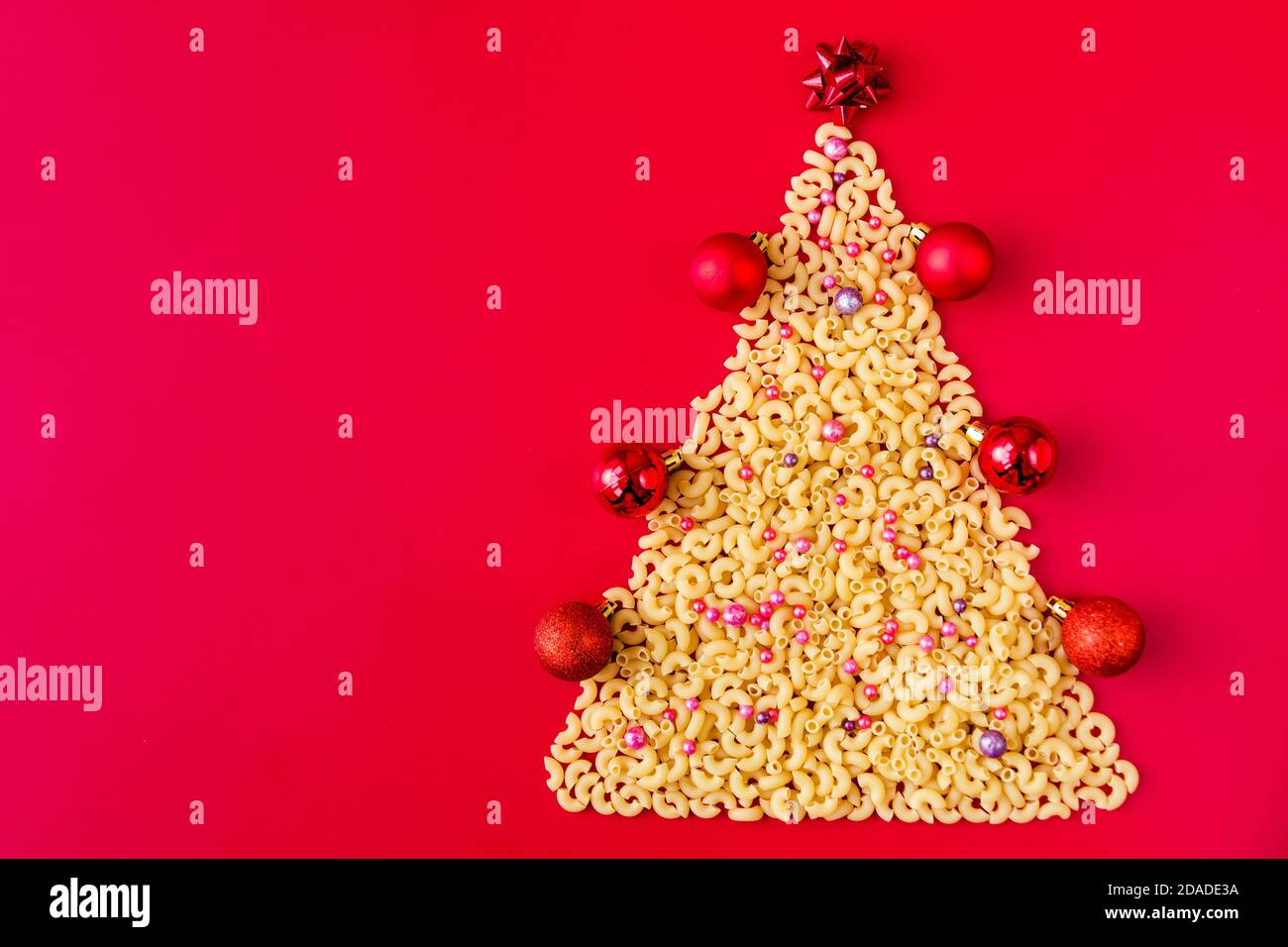 Arbre de Noël fait de pâtes italiennes crues avec des boules rouges isolées sur fond rouge.Concept vacances d'hiver Banque D'Images