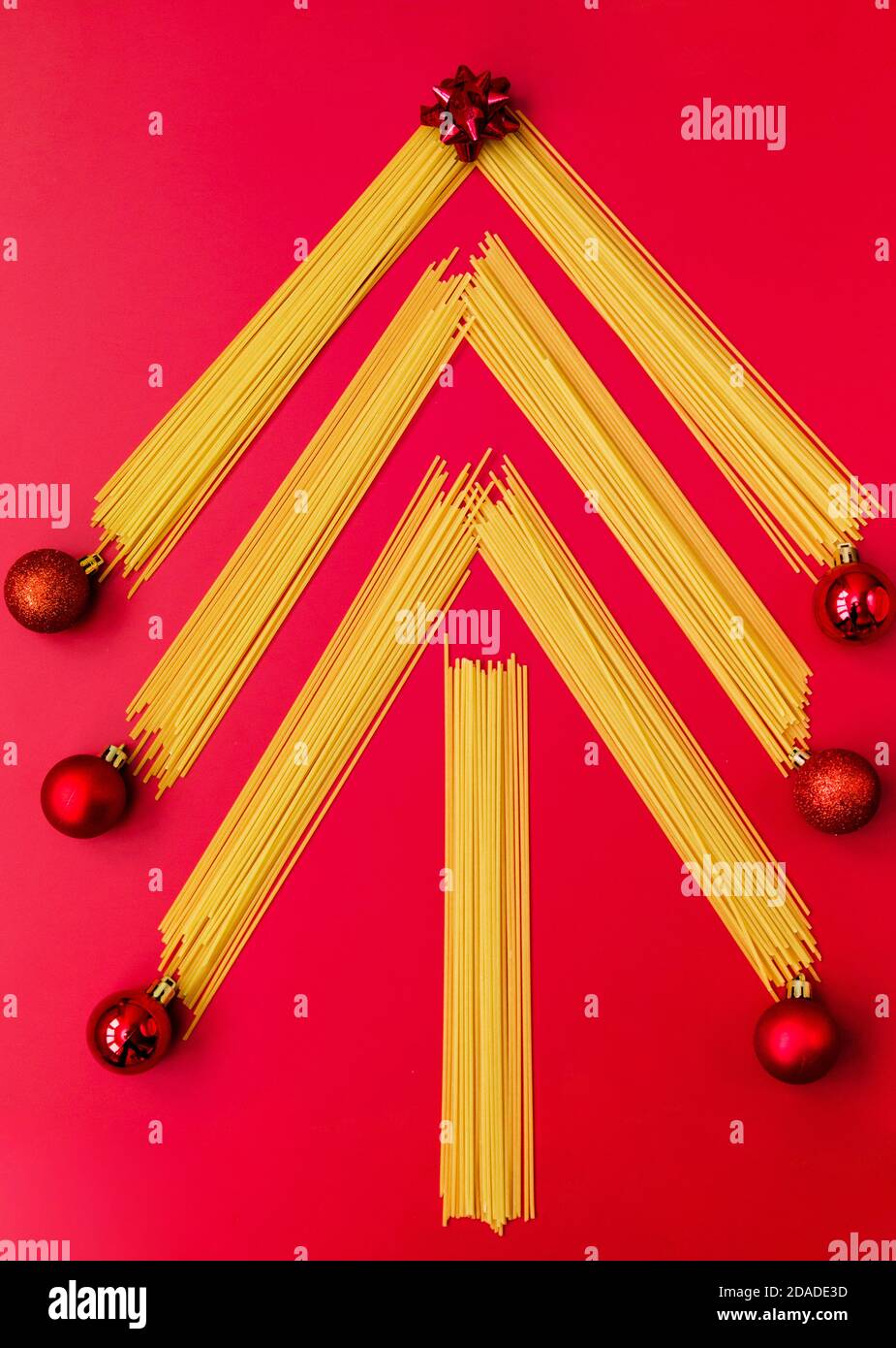 Arbre de Noël fait de pâtes italiennes crues avec des boules rouges isolées sur un fond rouge.Concept vacances d'hiver Banque D'Images