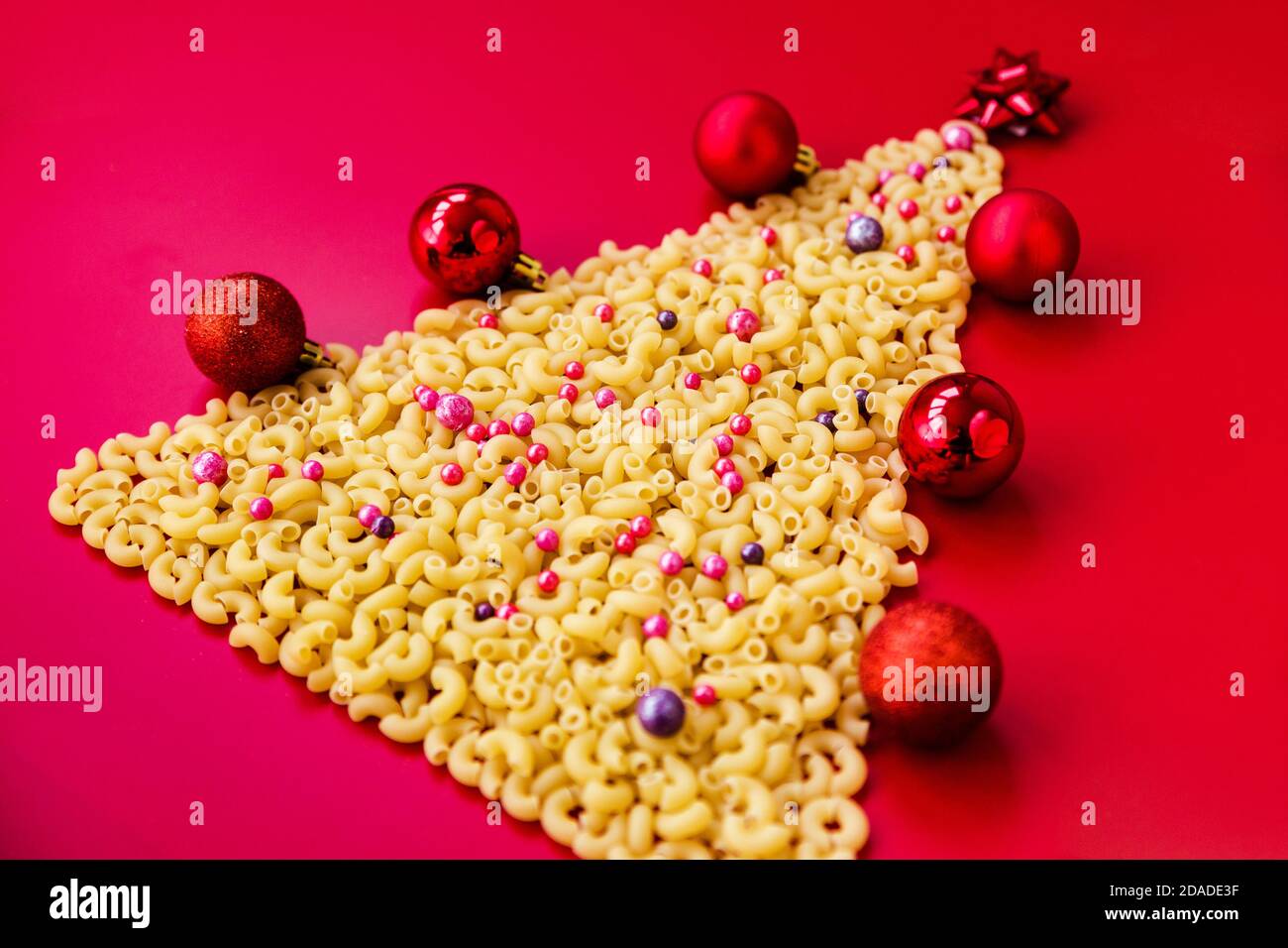 Arbre de Noël fait de pâtes italiennes crues avec des boules rouges isolées sur fond rouge.Concept vacances d'hiver Banque D'Images