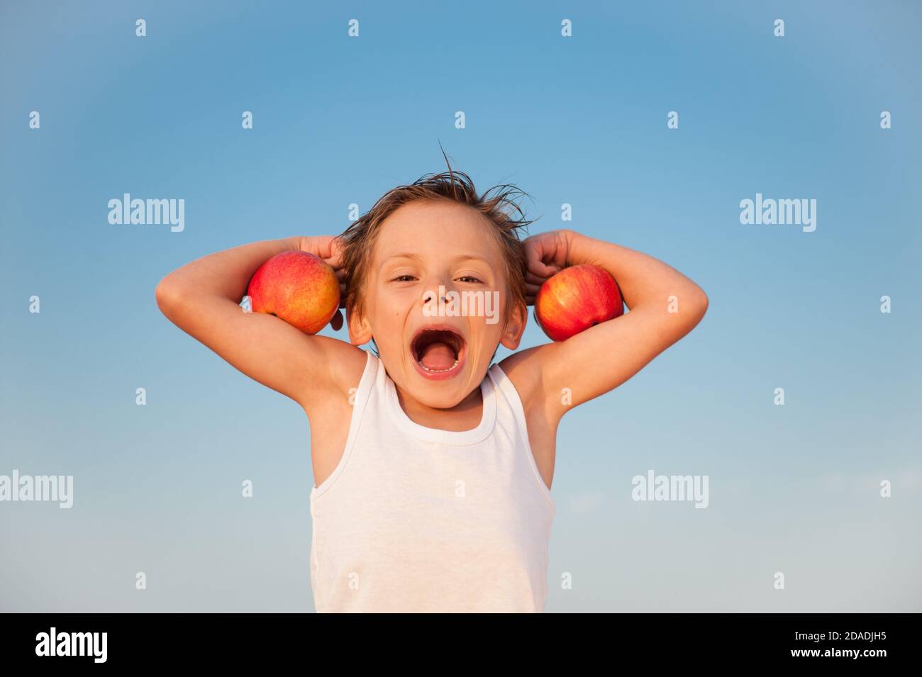 drôle d'enfant dans le réservoir blanc avec des pommes rouges dessus muscle biceps sur fond bleu ciel avec espace de copie Banque D'Images