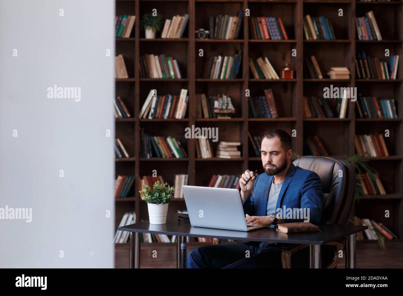 Un jeune homme d'affaires barbu dans le bureau de la bibliothèque est assis à un bureau . un homme travaille sur un ordinateur portable Banque D'Images