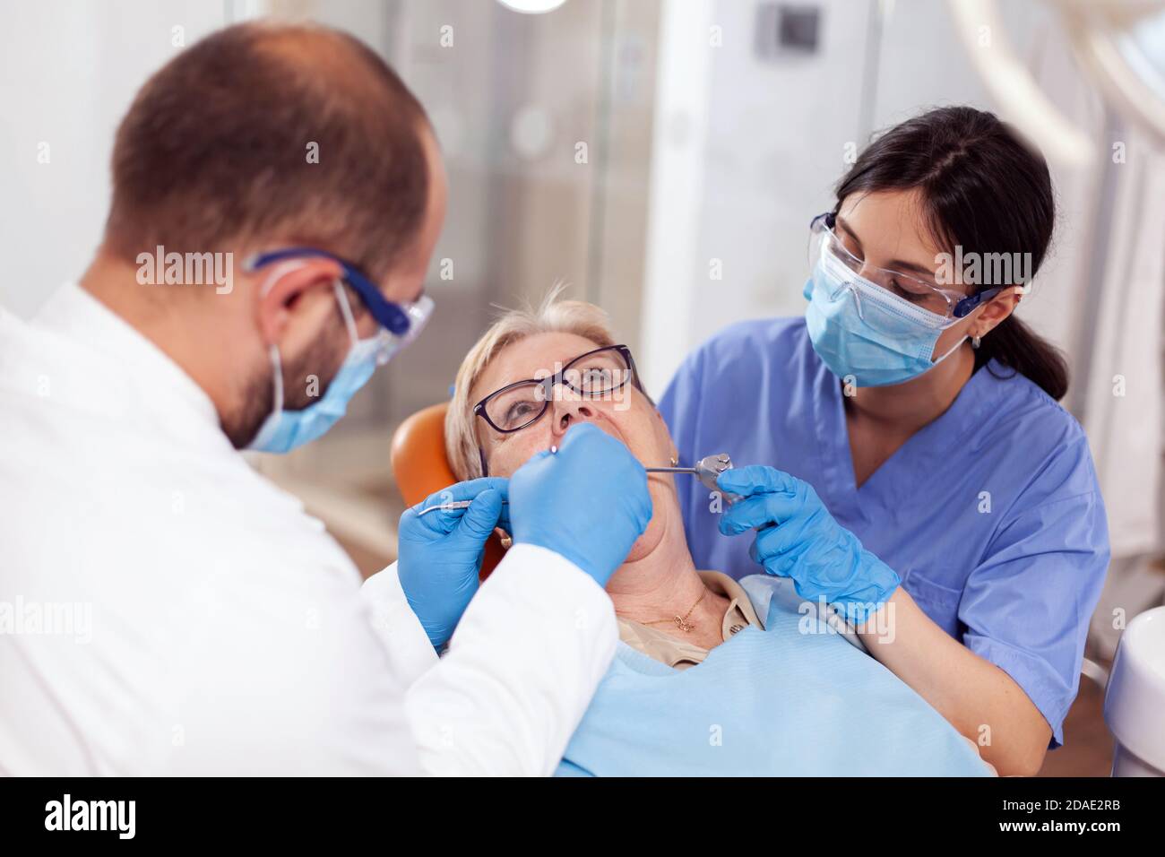 Stomatolog avec assistant de pose de joint dentaire sur les dents de femme âgée. Patient âgé pendant un examen médical avec un dentiste dans un cabinet dentaire équipé d'un équipement orange. Banque D'Images