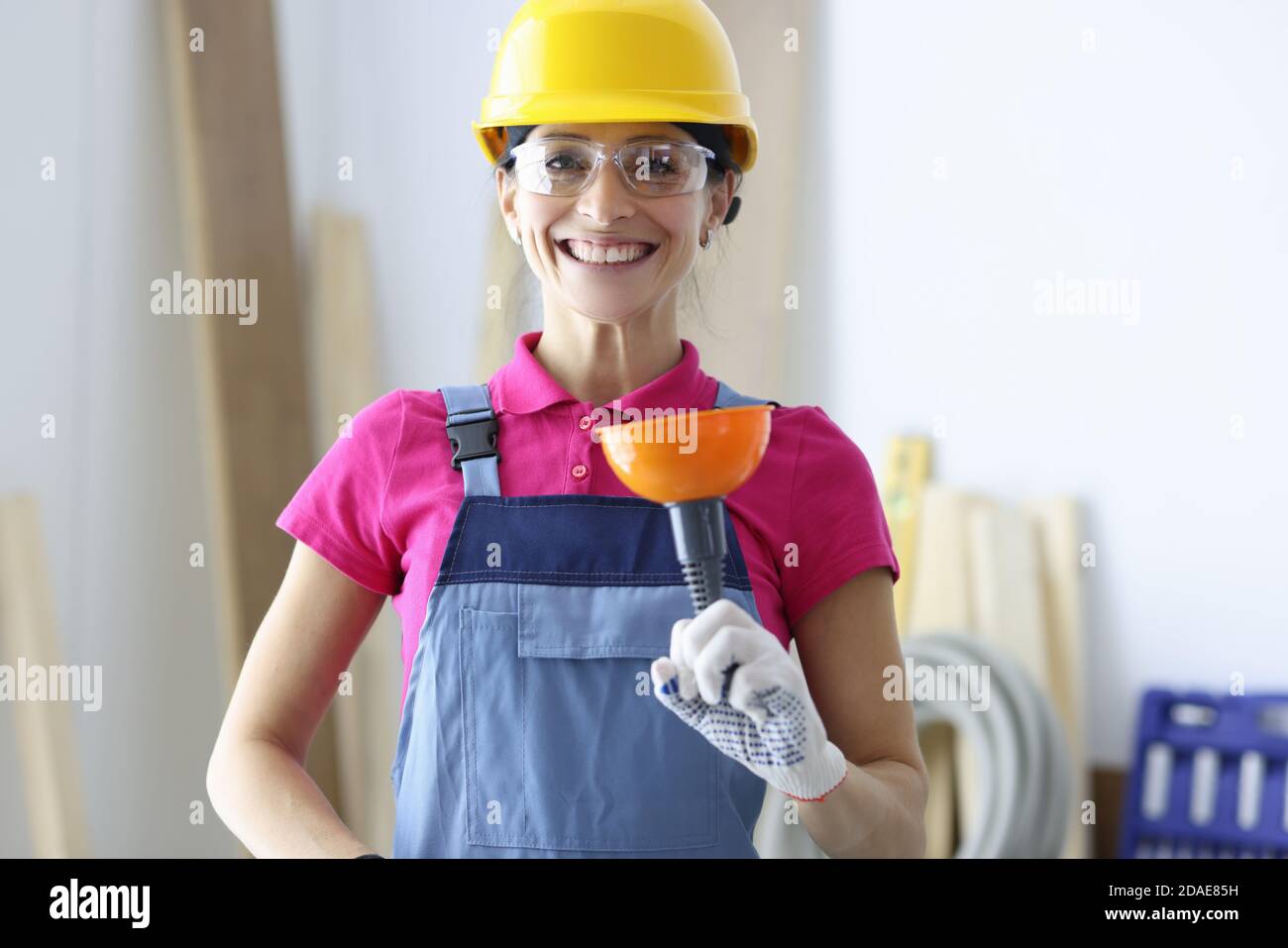 Femme souriante dans un casque de sécurité jaune et des lunettes tenant le piston en main Banque D'Images