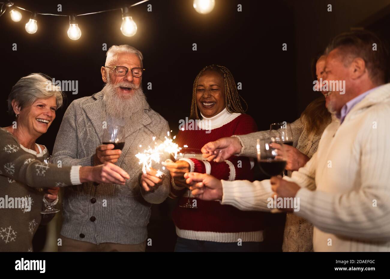 Les aînés heureux ayant le plaisir de célébrer les fêtes de boire du vin et de tenir feux d'artifice sparklers Banque D'Images