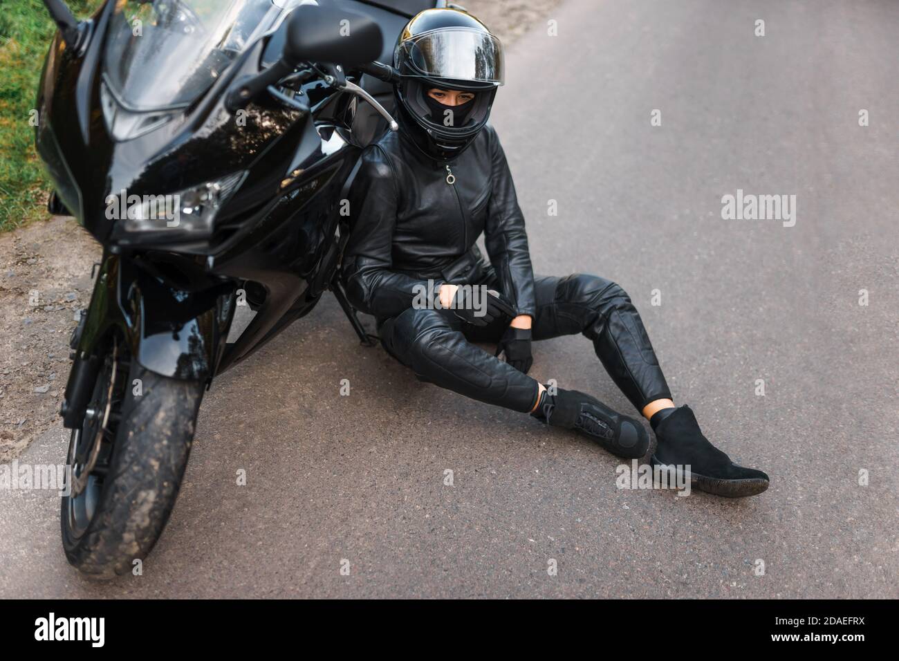 Une fille de motard en tenue noire se penche sur une moto Photo Stock Alamy