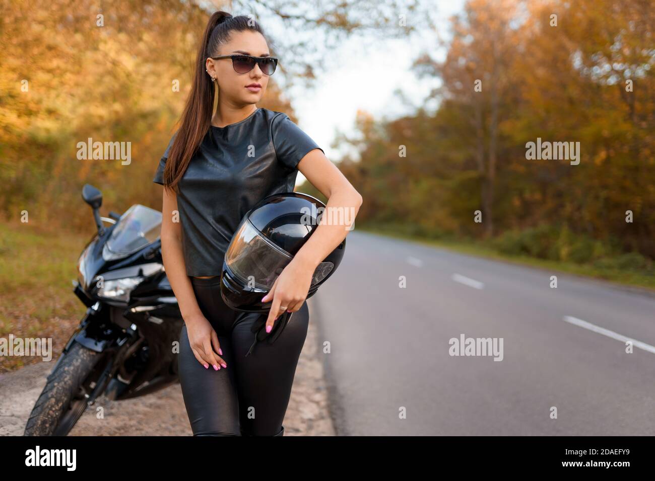 Femme brutale motard dans les lunettes se tient près de la moto sur le bord de la route et tenir le casque Banque D'Images