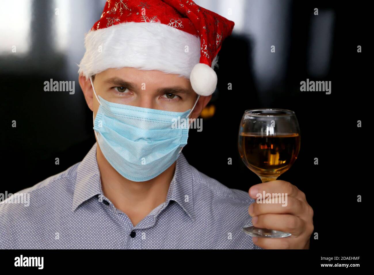 Homme dans le masque médical et chapeau du Père Noël avec un verre de vin en main. Célébration de Noël pendant la pandémie du coronavirus Banque D'Images