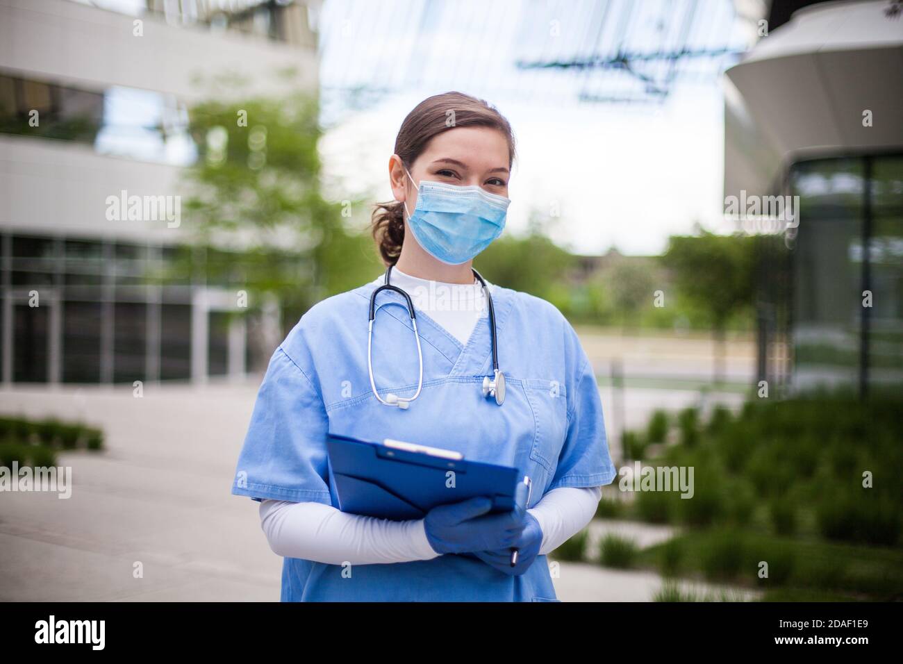 Femme médecin tenant un écritoire bleu debout à l'extérieur de l'hôpital ou de la clinique, en première ligne portrait d'un travailleur médical clé dans un établissement de soins moderne ou dans un établissement de soins infirmiers accueil Banque D'Images