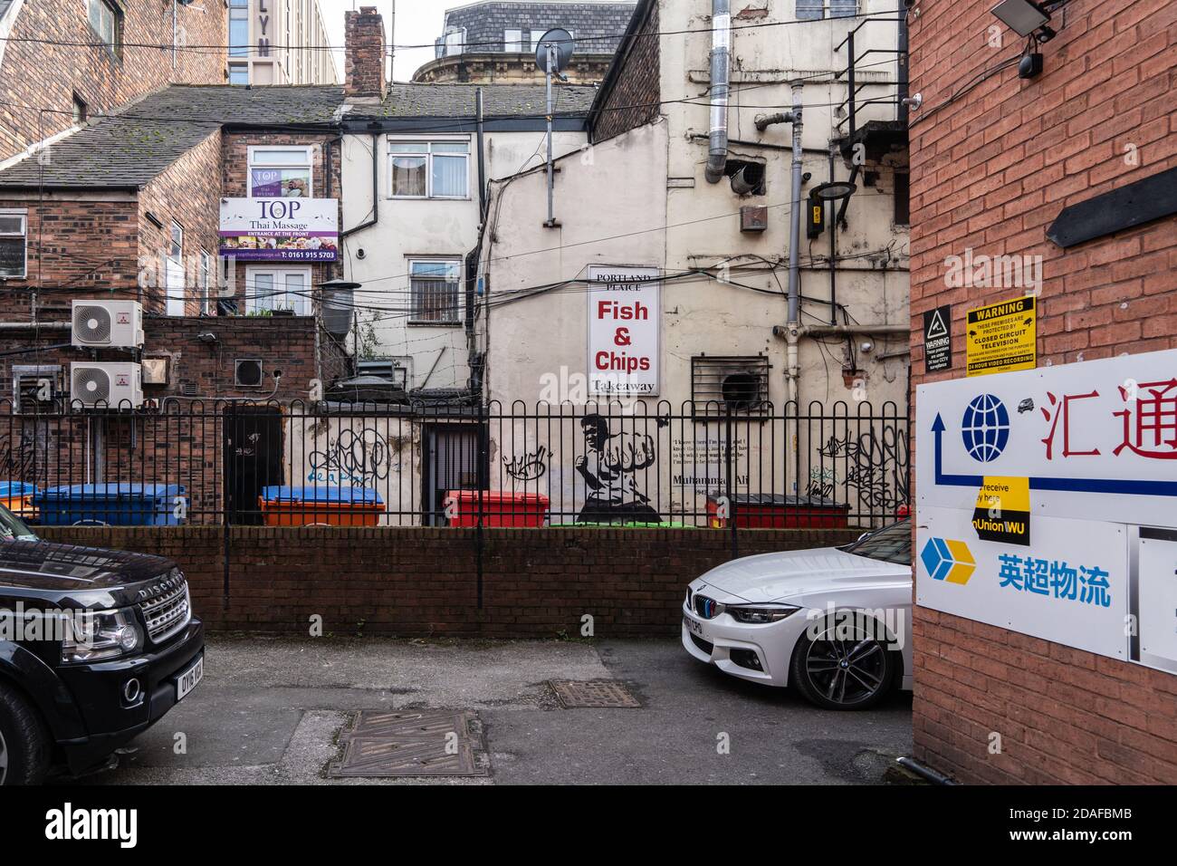 Parking avec écriture chinoise, dos de plusieurs maisons, panneaux et graffiti, dont un dessin de Muhammed Ali. Chinatown, Manchester Banque D'Images