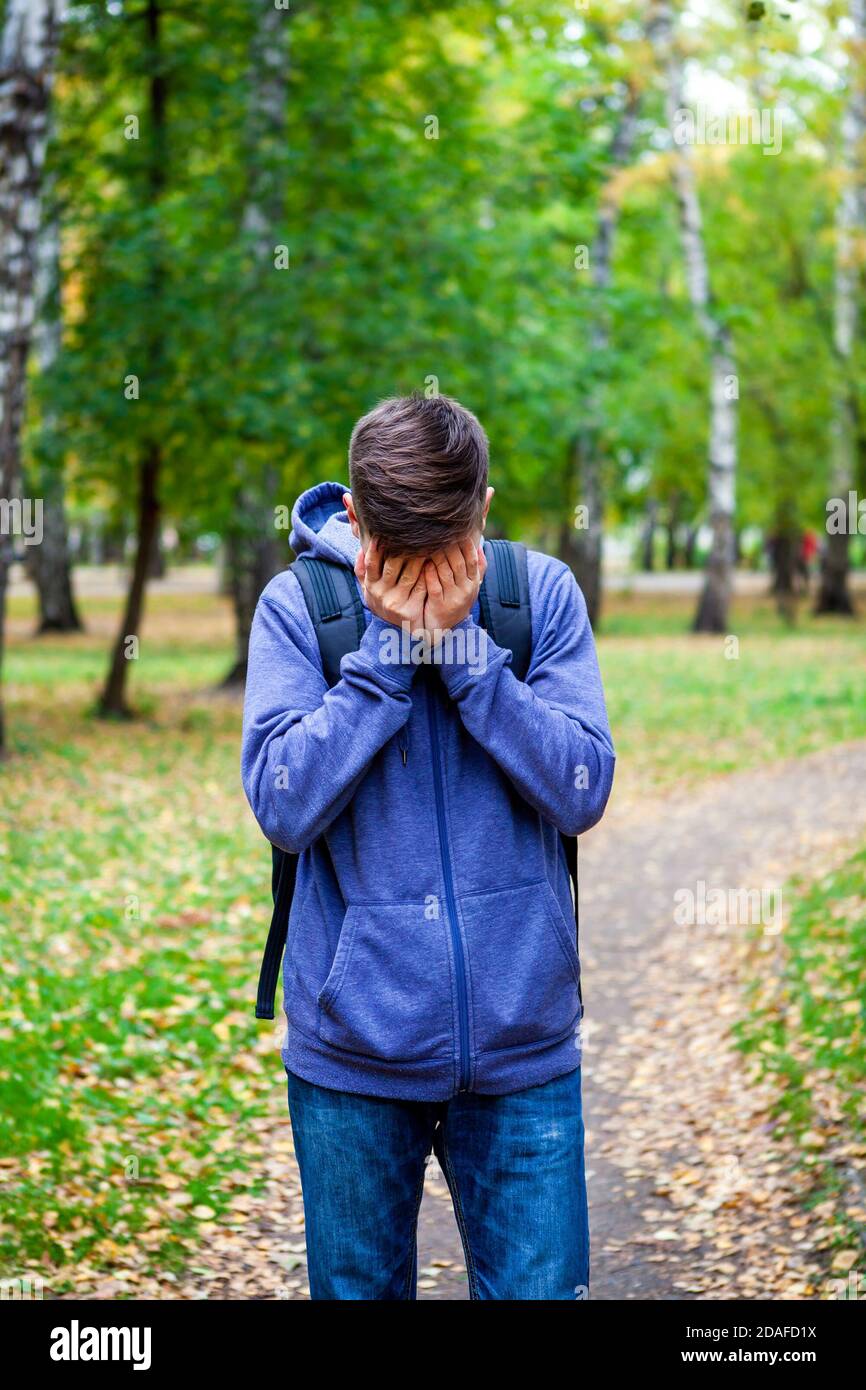 Le triste jeune homme cache son visage et pleure dans le Parc d'automne Banque D'Images