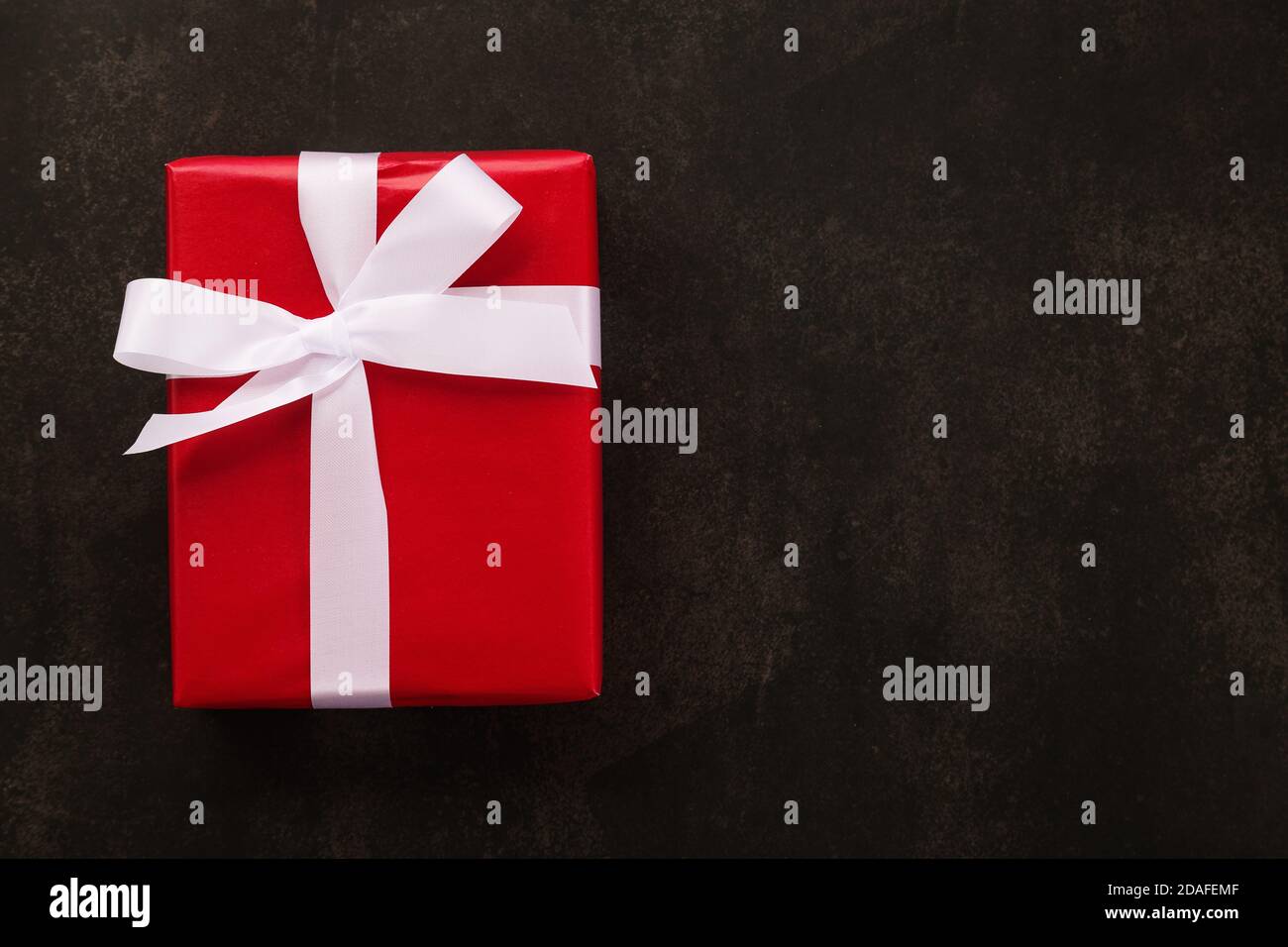 Vue de dessus de la boîte cadeau de Noël emballée de papier rouge et de ruban blanc sur fond de grunge. Banque D'Images Vue de dessus de la boîte cadeau de Noël emballée de papier rouge et de ruban blanc sur fond de grunge. Banque D'Images